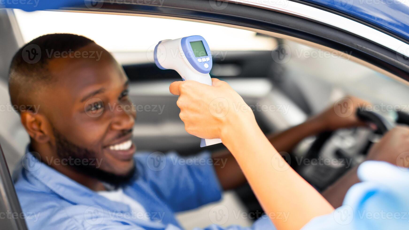 New Normal, Control, Pandemic, Covid-19 on Road in Transit. Medical worker measuring temperature of young black male driver through car window before leaving quarantine zone or crossing country border photo