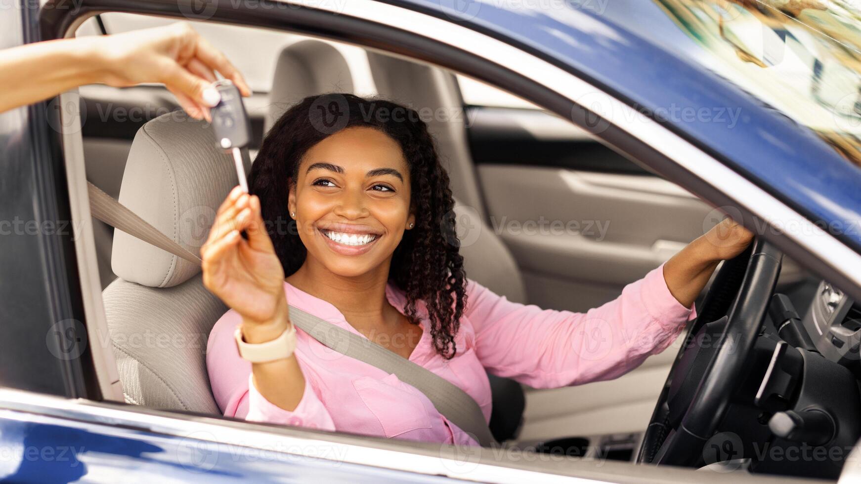 Car Sales. Manager giving new auto key to happy young black lady at dealership store, selective focus. Excited African American customer buying vehicle from salesman seller at automobile showroom photo