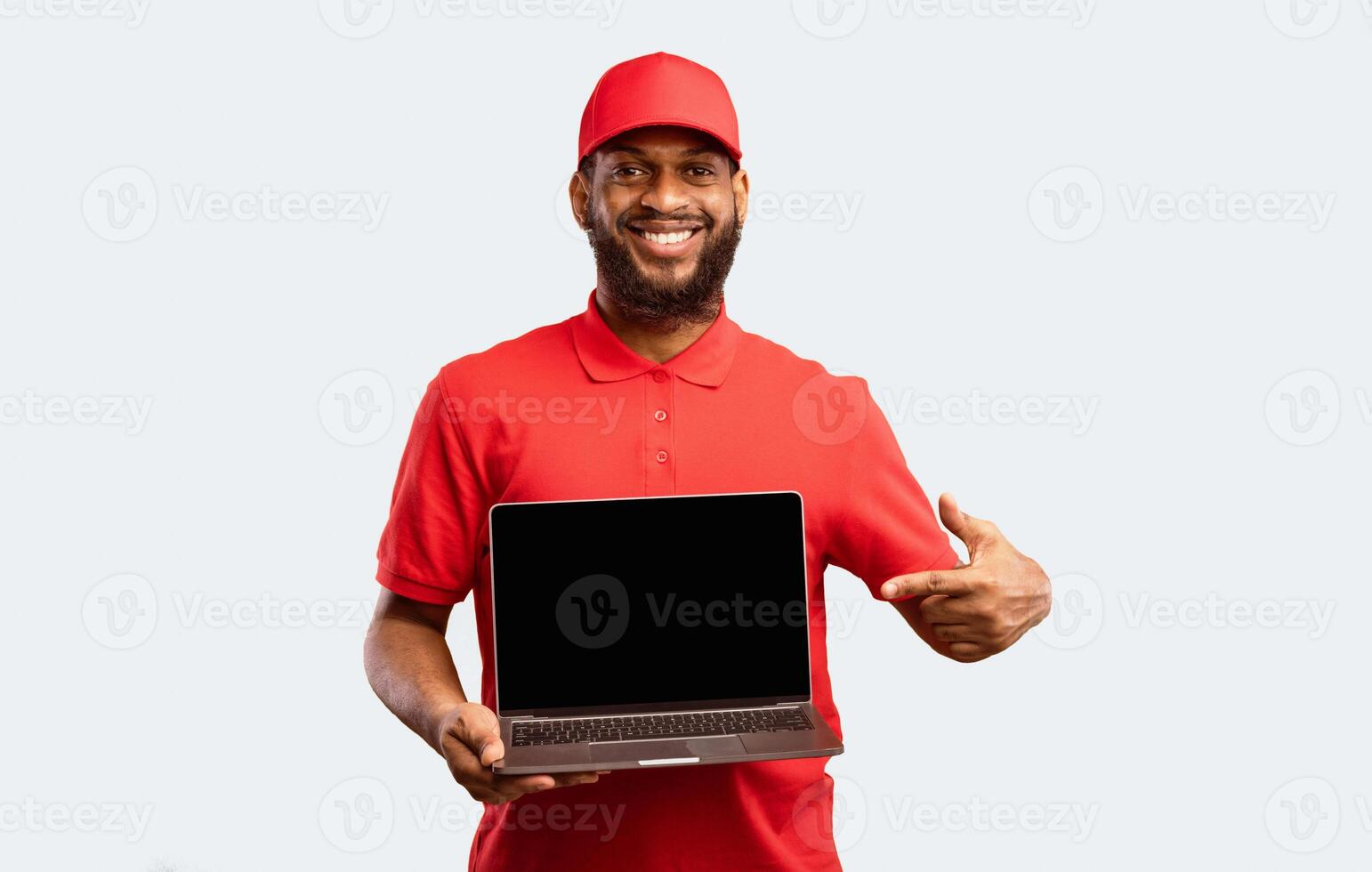 Delivery Service. Courier Holding Laptop With Blank Screen Smiling To Camera On Yellow Studio Background Advertising Shipping Service. Mockup photo