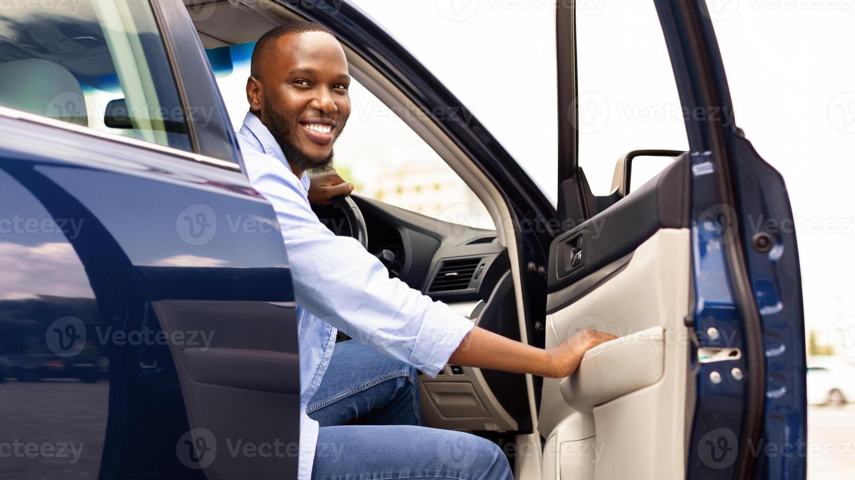 Positive young African American guy going out the car, looking for fellow traveler. Happy black man open automobile door and smiling, getting in. Auto test-drive, leasing, buying, rent concept photo