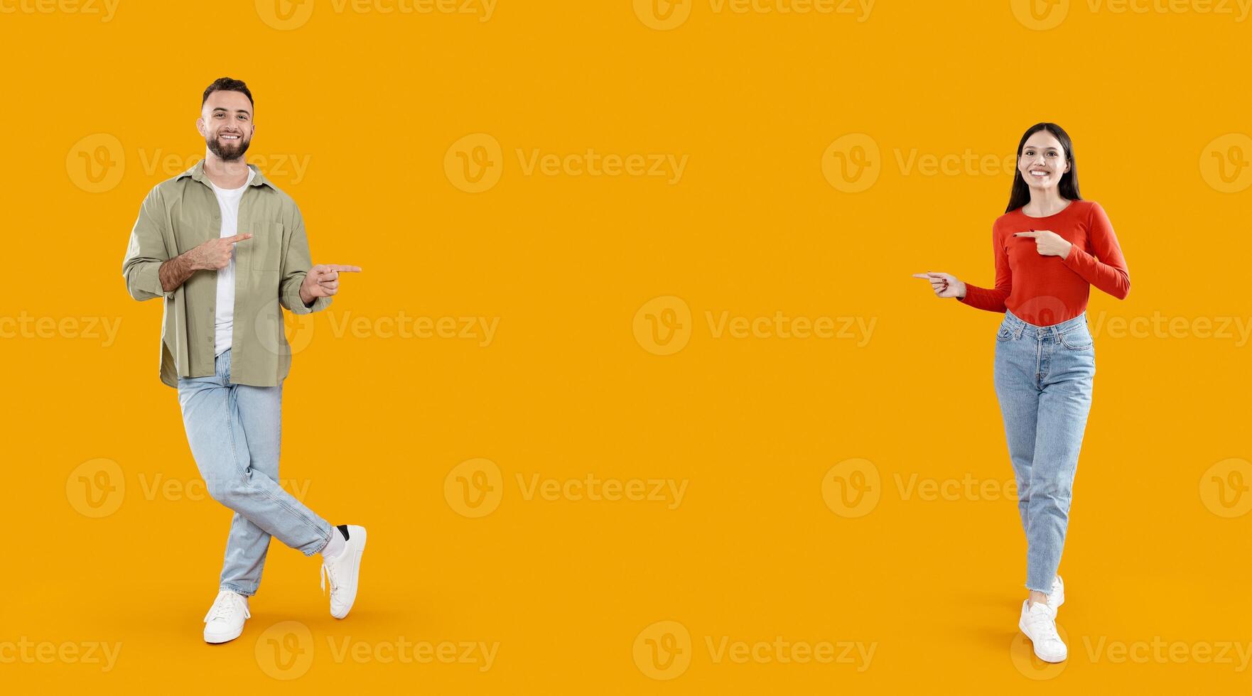 A happy couple stands together in a bright yellow background, playfully pointing at copy space between them. Their joyful expressions reflect a moment of togetherness and love. photo