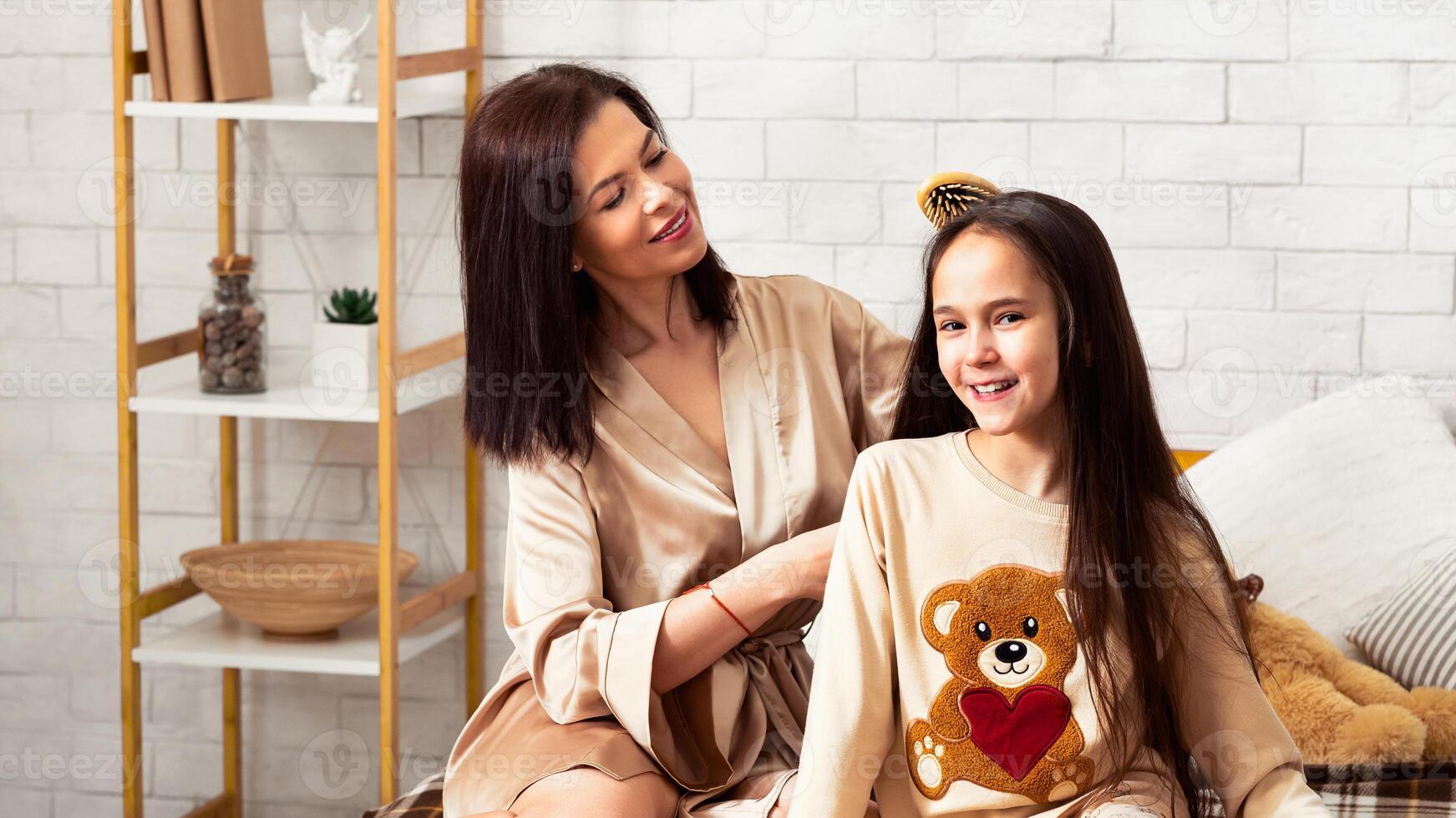 Wellness day. Happy mother brushing her daughter's hair on bed at home. Panorama photo