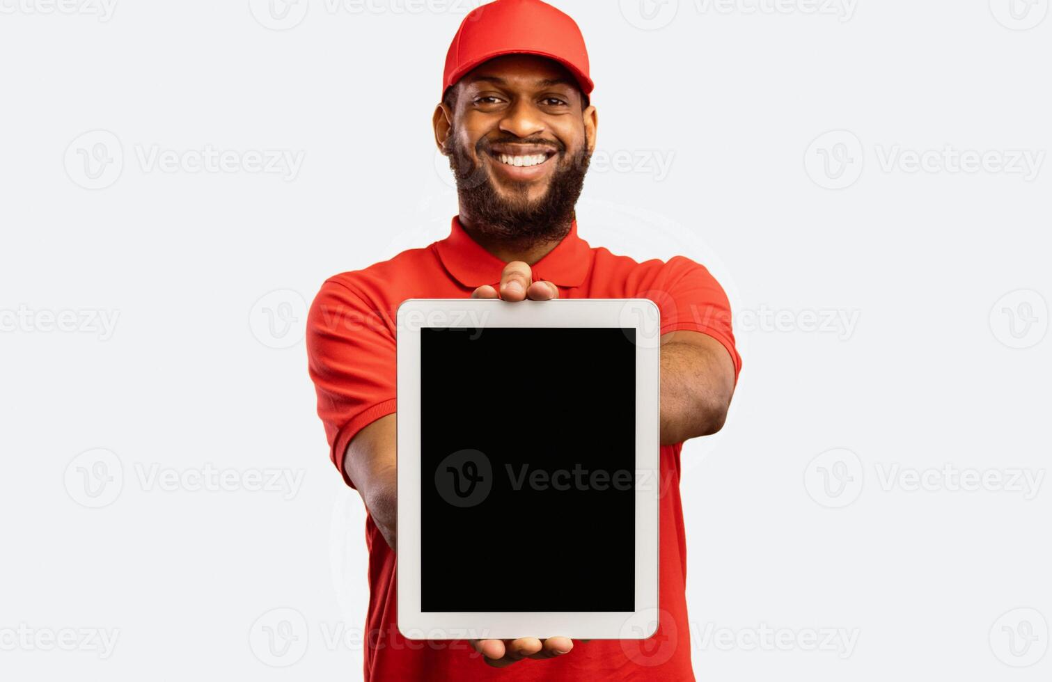 Cheerful Delivery Man Showing Digital Tablet Empty Screen Recommending Postal Courier Service Standing On Yellow Background. Mockup photo