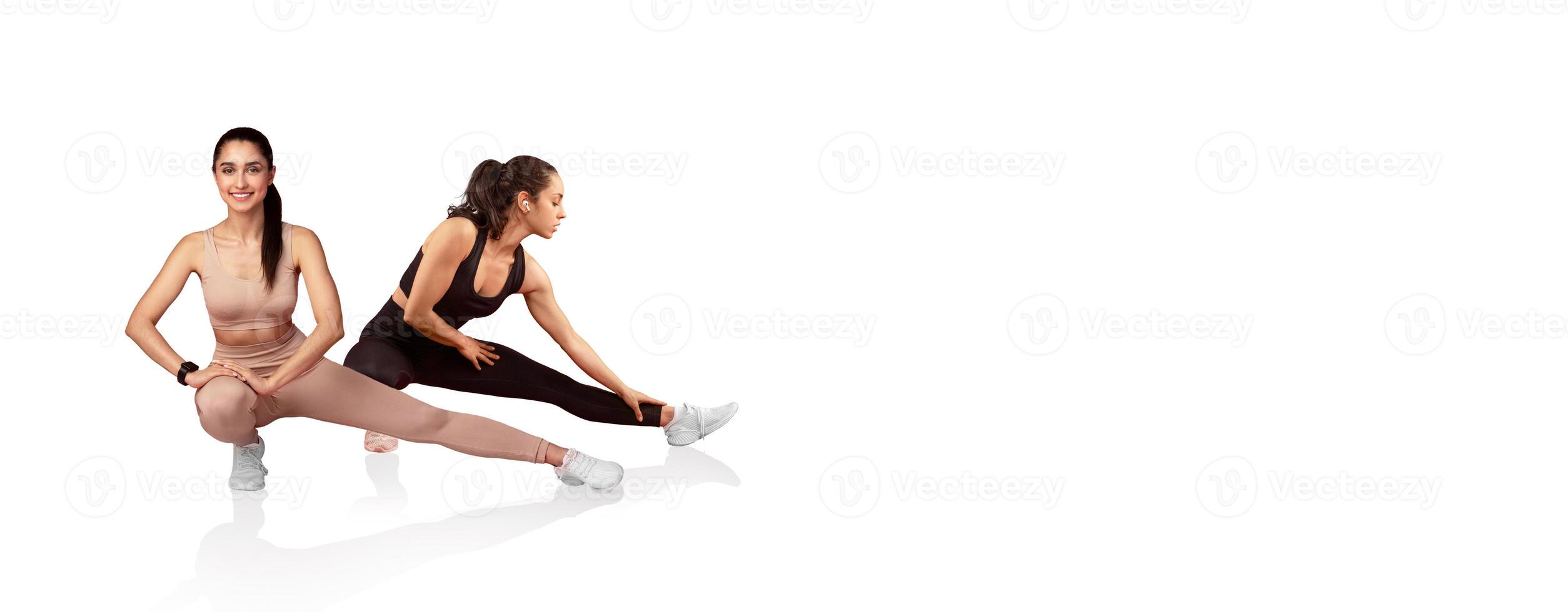 Two women engage in dynamic stretching exercises, focusing on flexibility and warm-up. They wear comfortable athletic outfits and showcase various stretching techniques in a bright space. photo