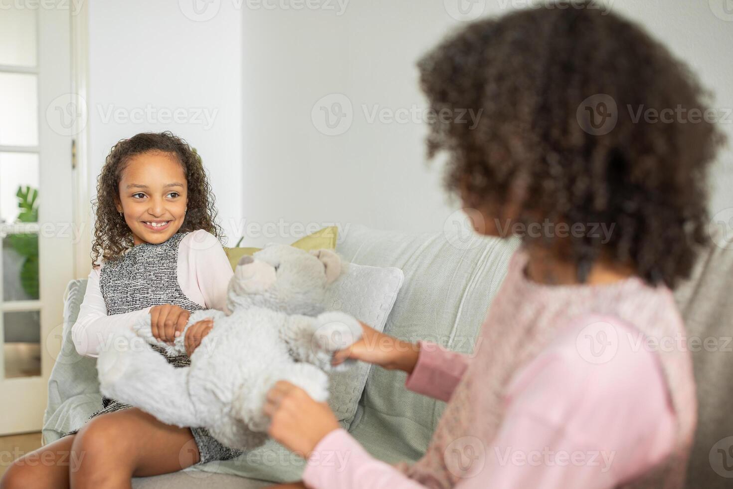 Sisters share a playful moment on the couch as they engage with a soft toy, showcasing love and affection in their comfortable family home environment. photo