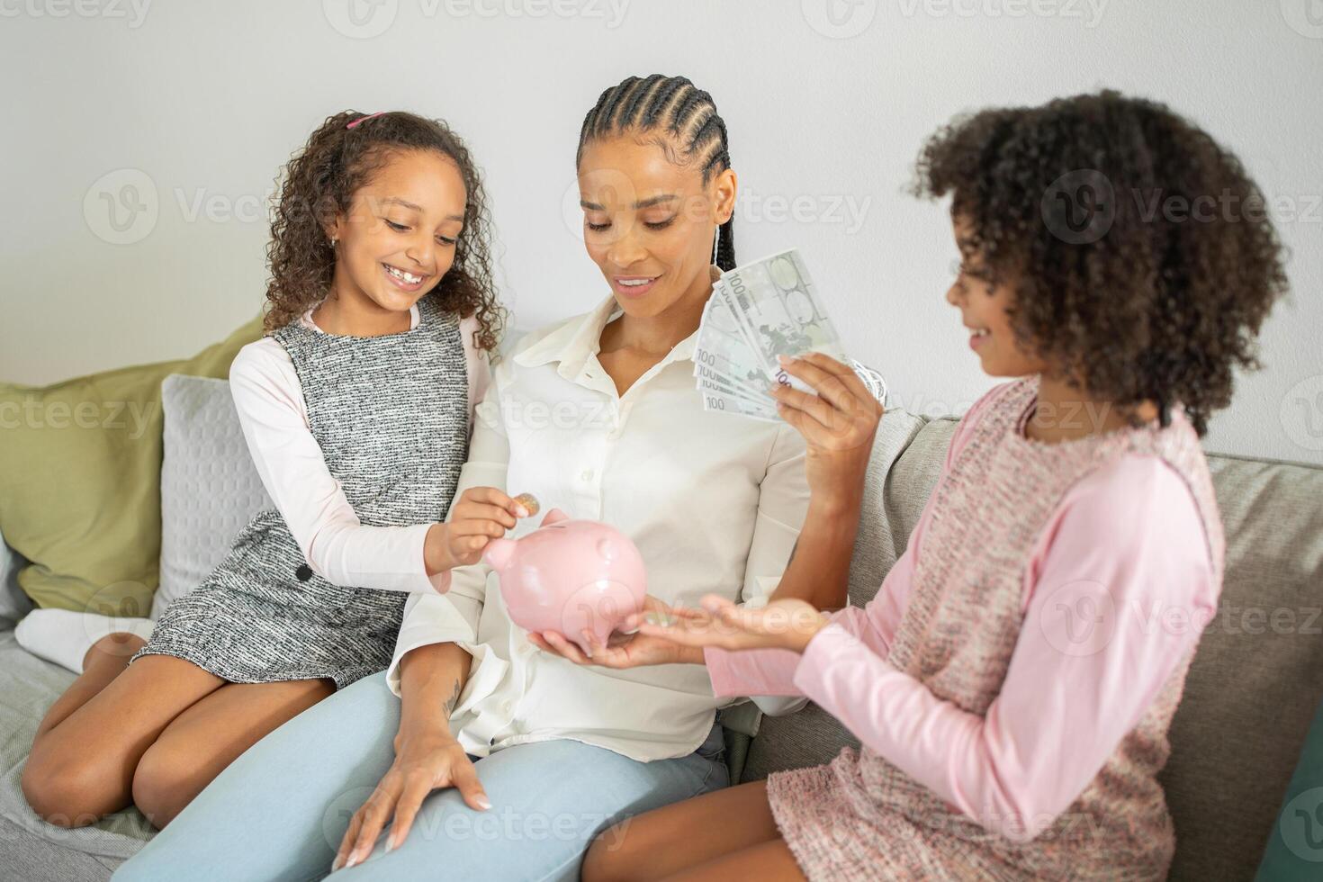 A mother sits on a couch with her two daughters, teaching them about savings using a piggy bank. The atmosphere is warm and affectionate, highlighting family togetherness. photo