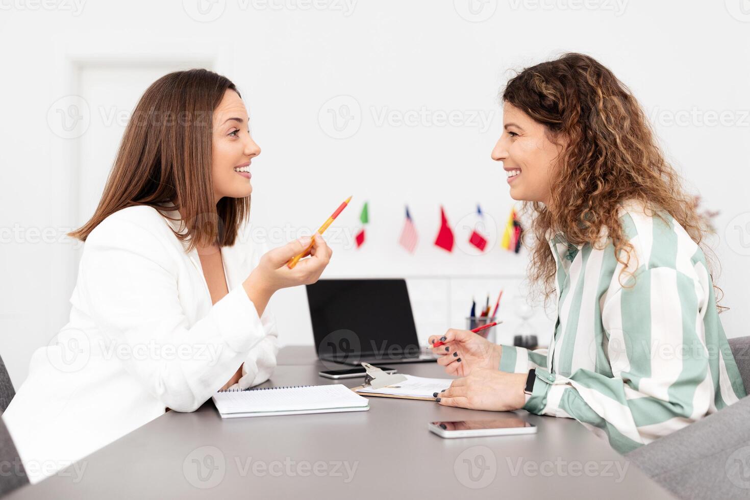 Two Caucasian women engage in a collaborative discussion at a corporate office. They share ideas while reviewing documents, showcasing teamwork among millennials. photo