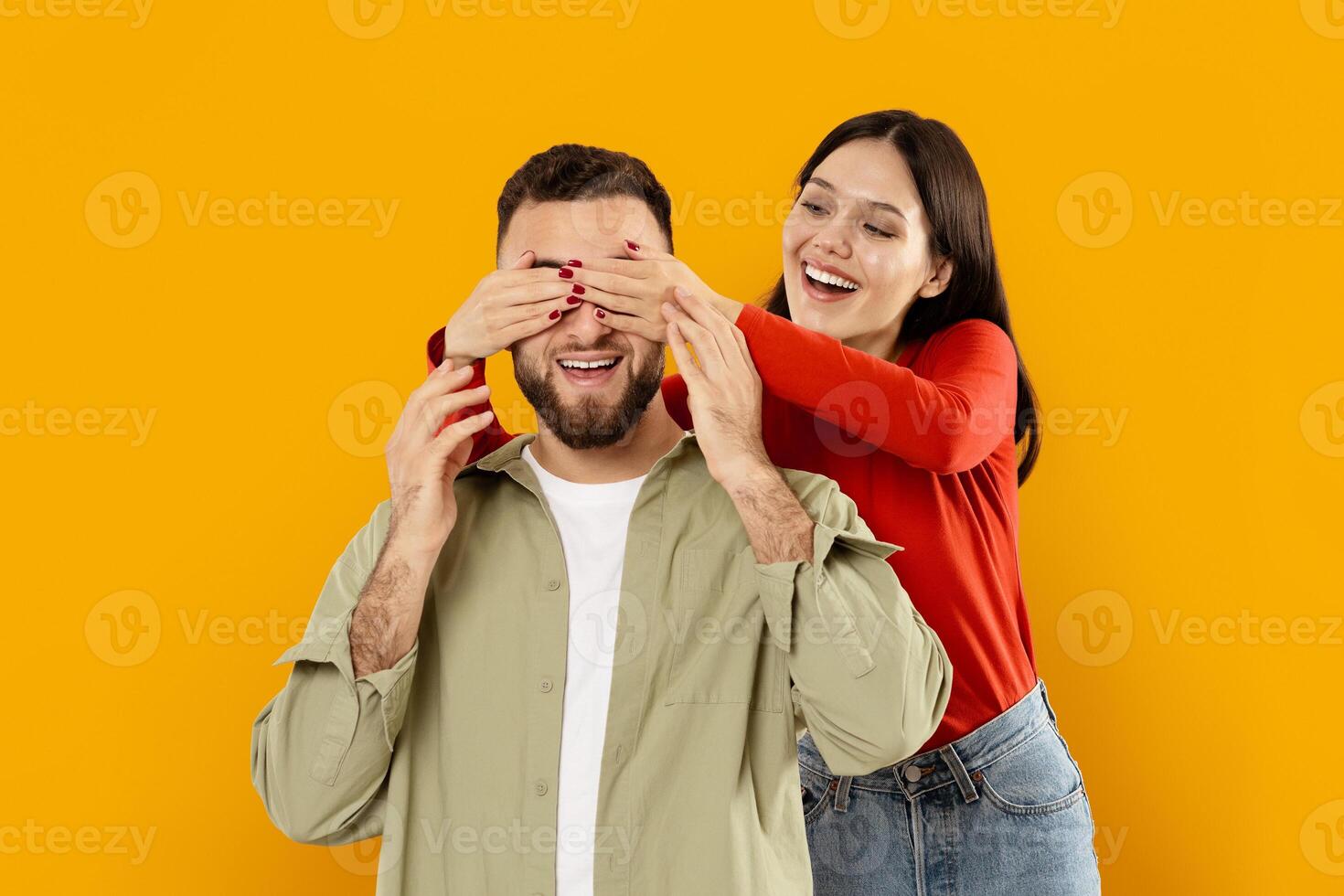 A young couple enjoys a light-hearted moment as one partner playfully covers the other's eyes with their hands, showcasing their affection and connection against a bright yellow backdrop. photo