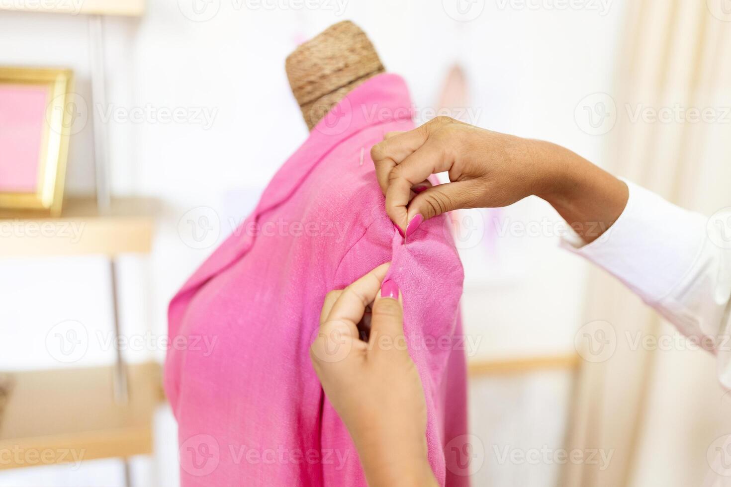 A middle aged Hispanic woman carefully stitches and adjusts a bright pink garment on a mannequin in a well-lit design studio. Her focused expression shows her dedication to her craft. photo
