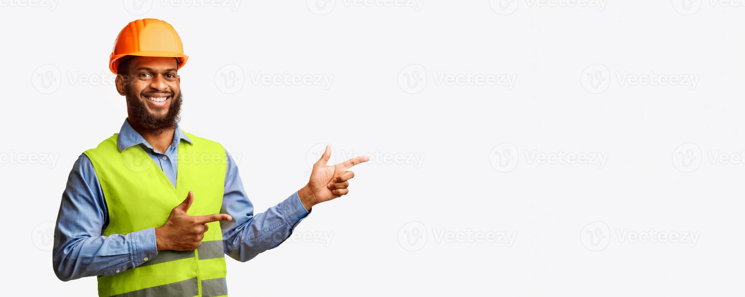 Smiling African Builder Guy In Uniform Pointing Fingers Aside At Free Space Standing On White Studio Background. Panorama photo