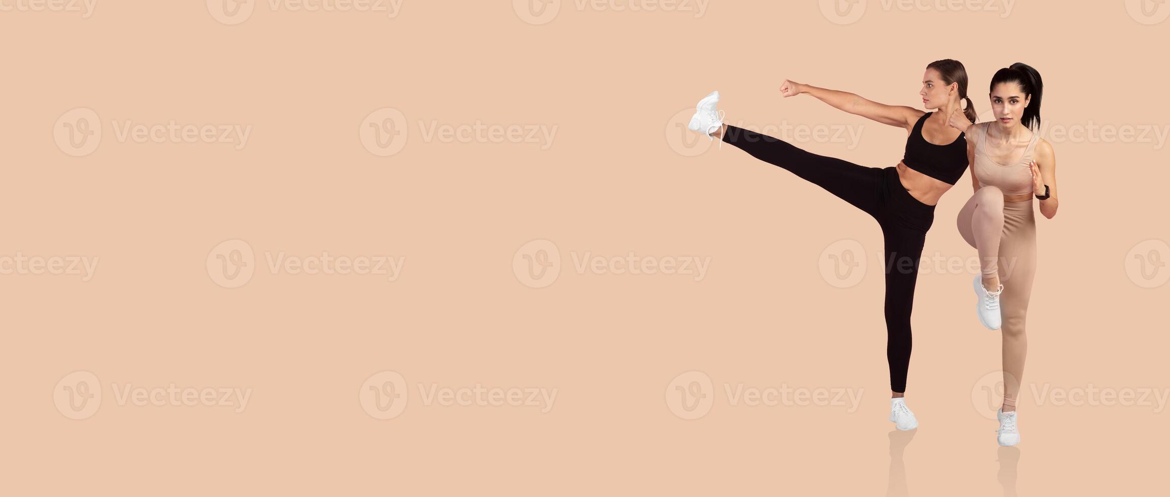 Two women are engaged in an energetic workout, showcasing synchronized fitness routines. They are dressed in activewear, with a bright, neutral background highlighting their movements. photo