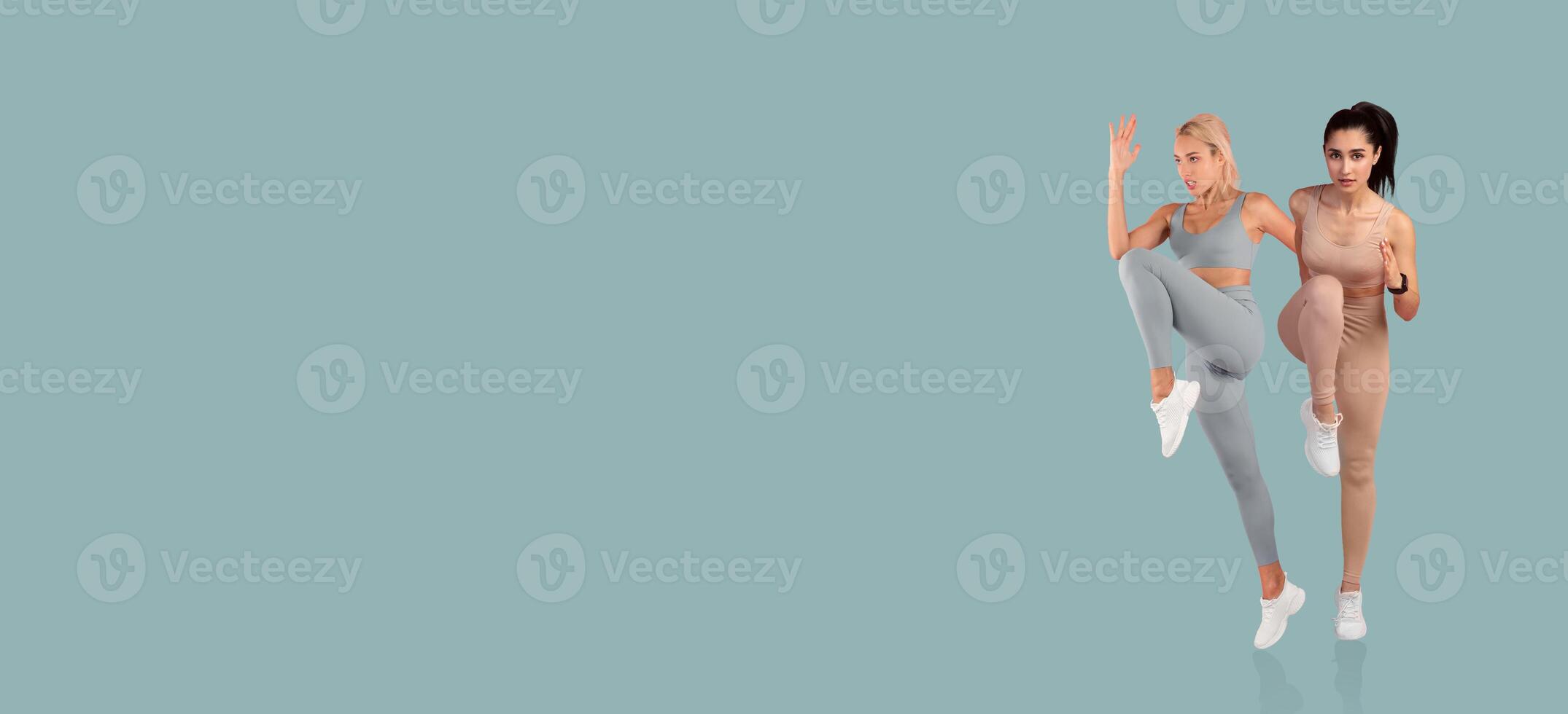 Two women are engaged in a workout, demonstrating fitness poses while wearing matching leggings. The backdrop is a solid color, highlighting their movements and focus on exercise. photo