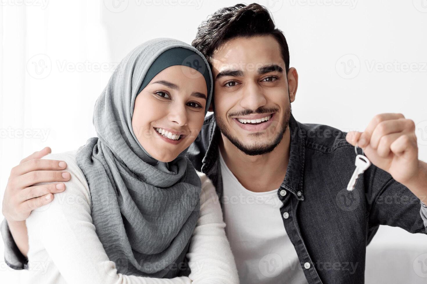 Happy muslim family leaning on paper boxes and showing keys from their new apartment. Handsome arab man and young woman in hijab moving to their house, unpacking belongings, copy space photo