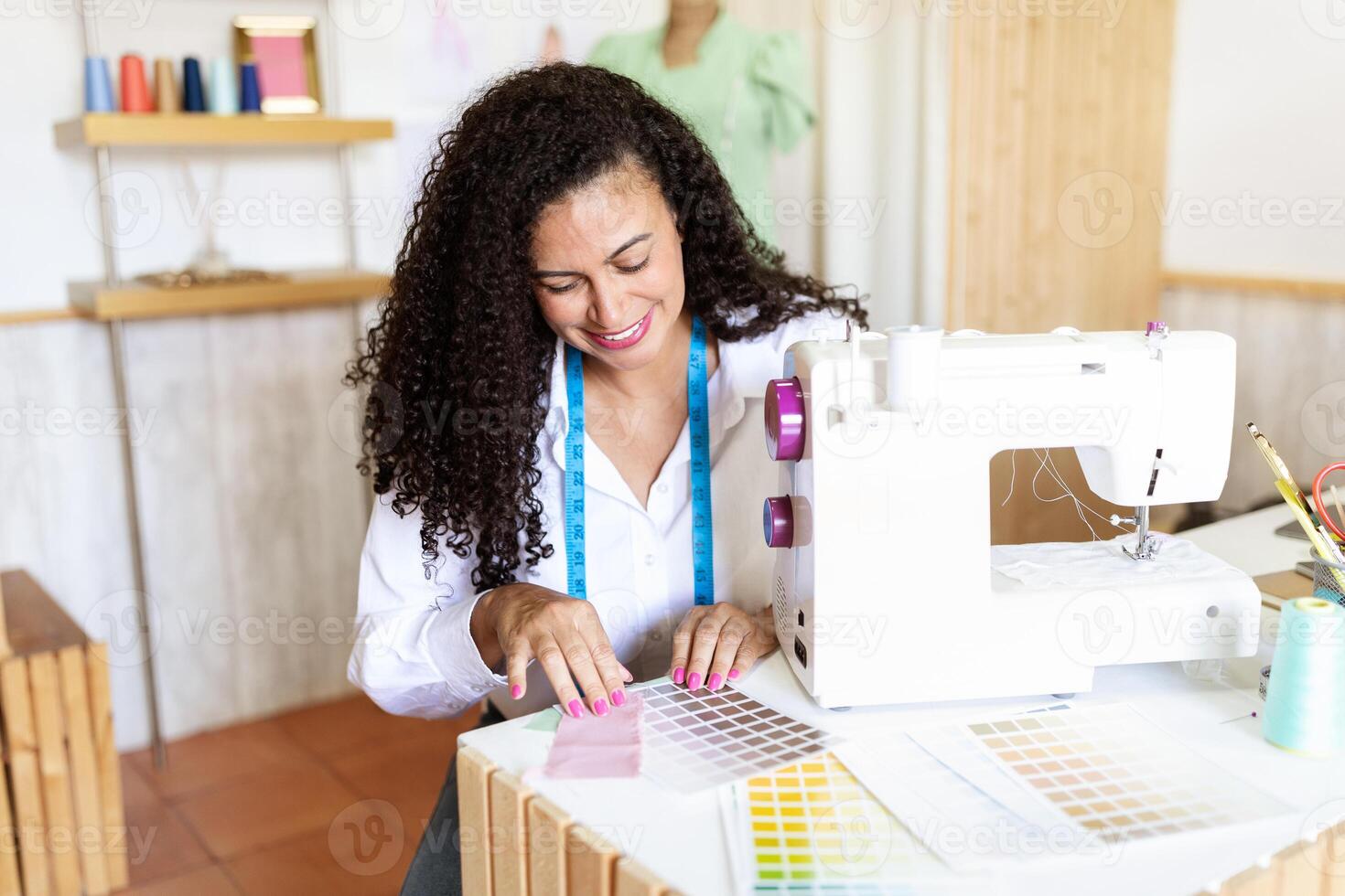 A middle aged Hispanic woman is focused on her work, arranging fabric swatches at her sewing machine in a well-lit office setting filled with colorful sewing supplies. photo