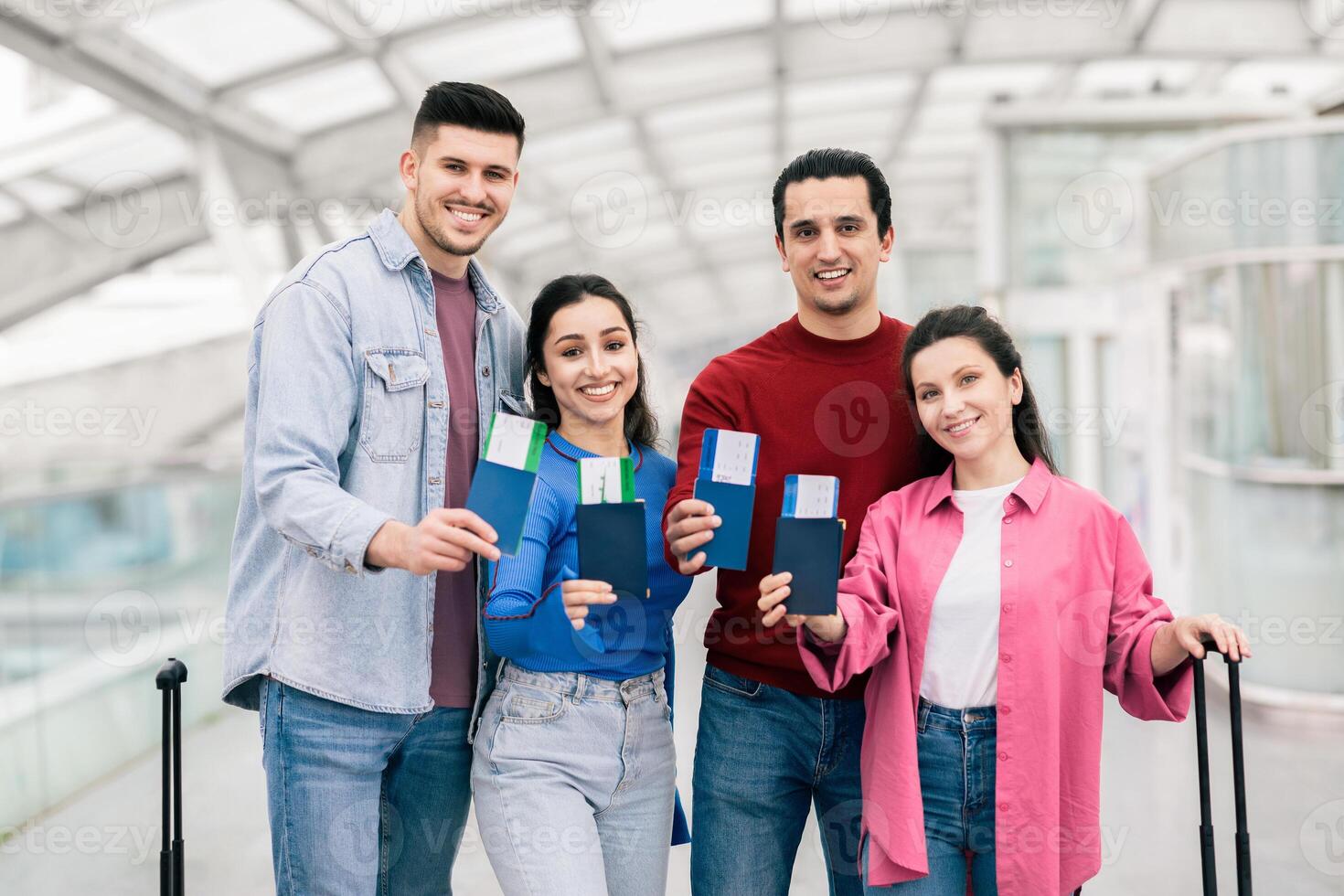 A group of two couples holds their travel documents, smiling in an airport. They appear excited for their vacation together, showcasing a moment of joy and adventure indoors before departure. photo