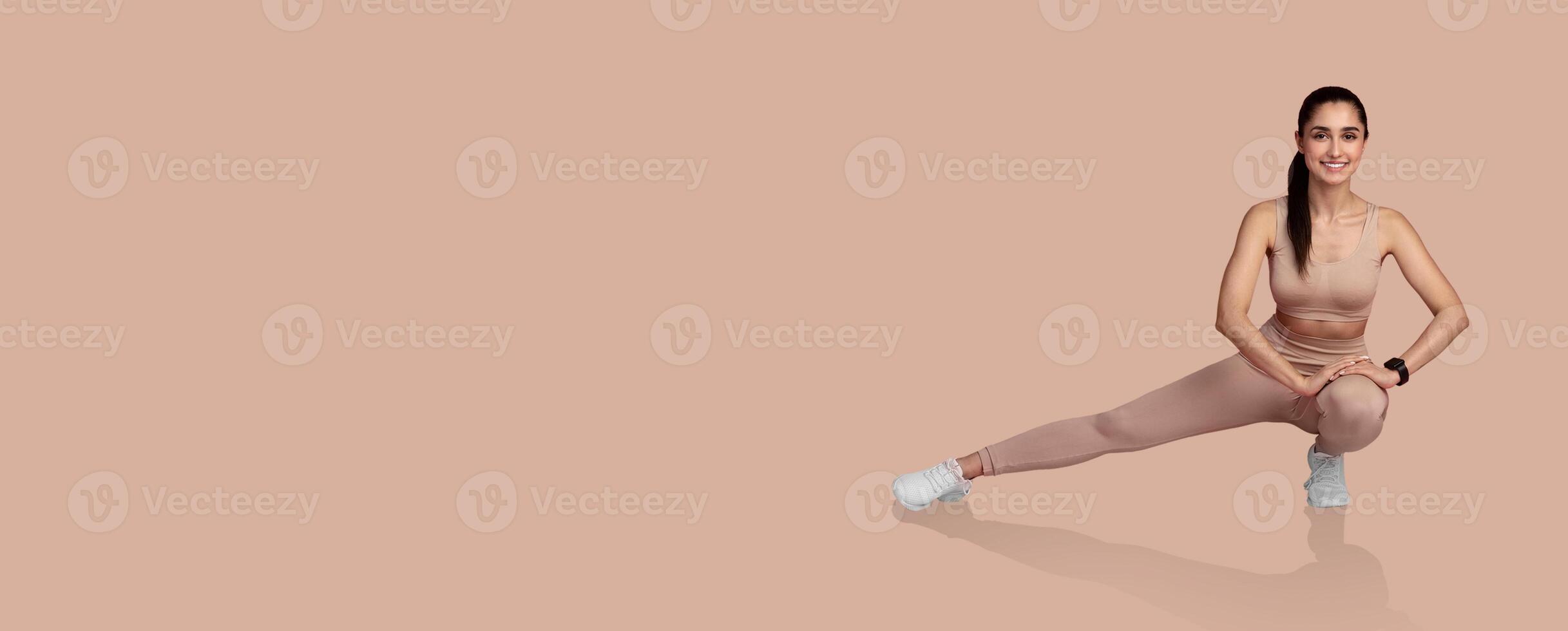 A woman performs a dynamic leg stretch, showcasing flexibility and strength. She wears form-fitting activewear and focuses on her exercise routine in a minimalist setting. photo