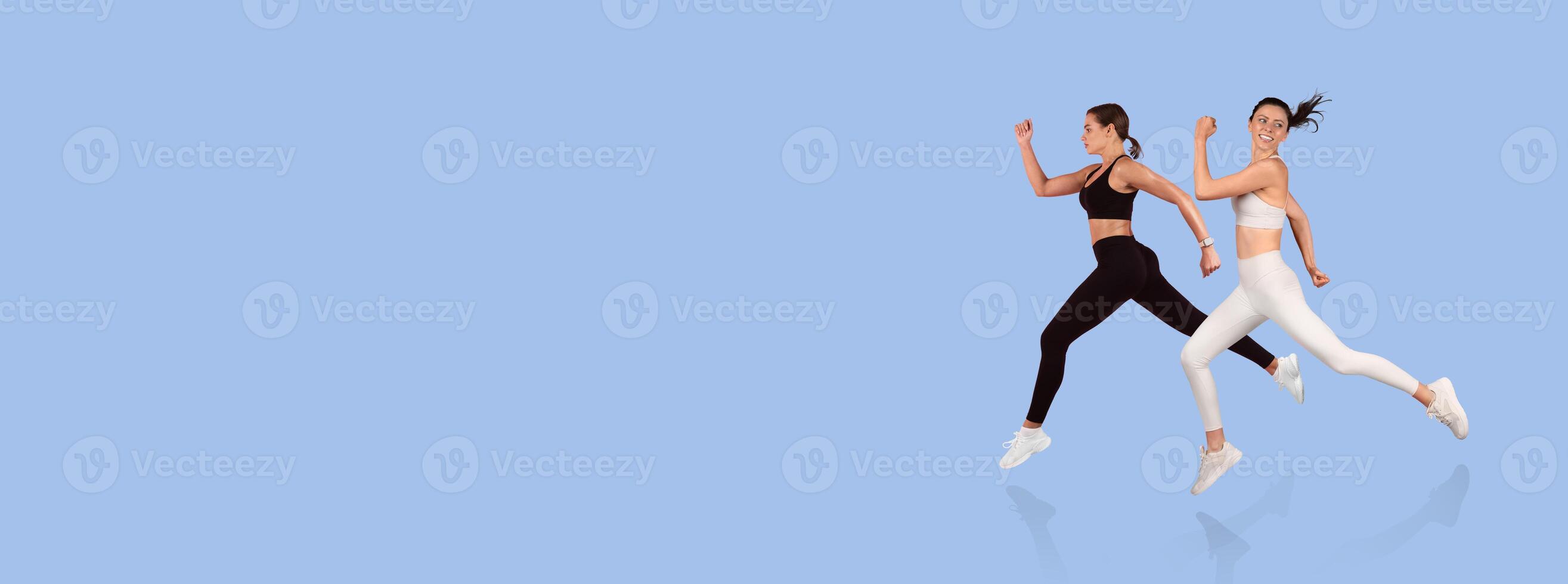 Two women are captured mid-run, dressed in stylish athletic outfits, showcasing fitness and movement against a vibrant blue backdrop. Their energetic poses exude strength and determination. photo