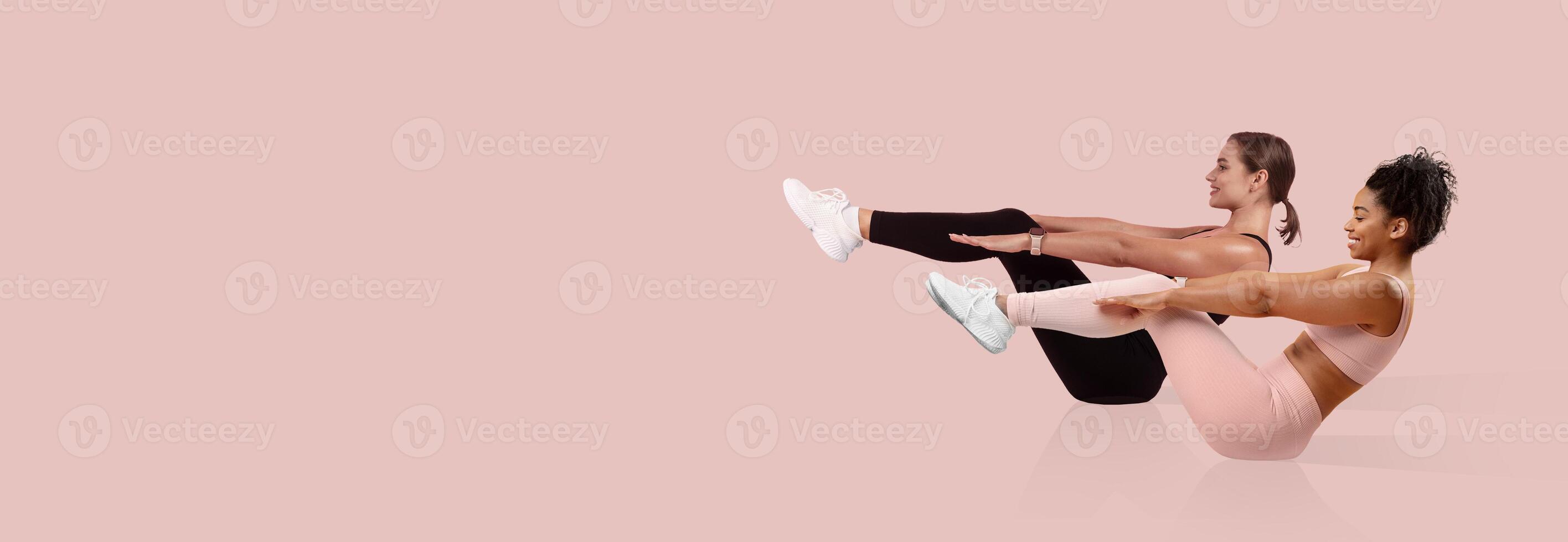 Two women engage in synchronized core exercises on a pink backdrop, demonstrating flexibility and strength. Both are focused and determined while showcasing proper form. photo