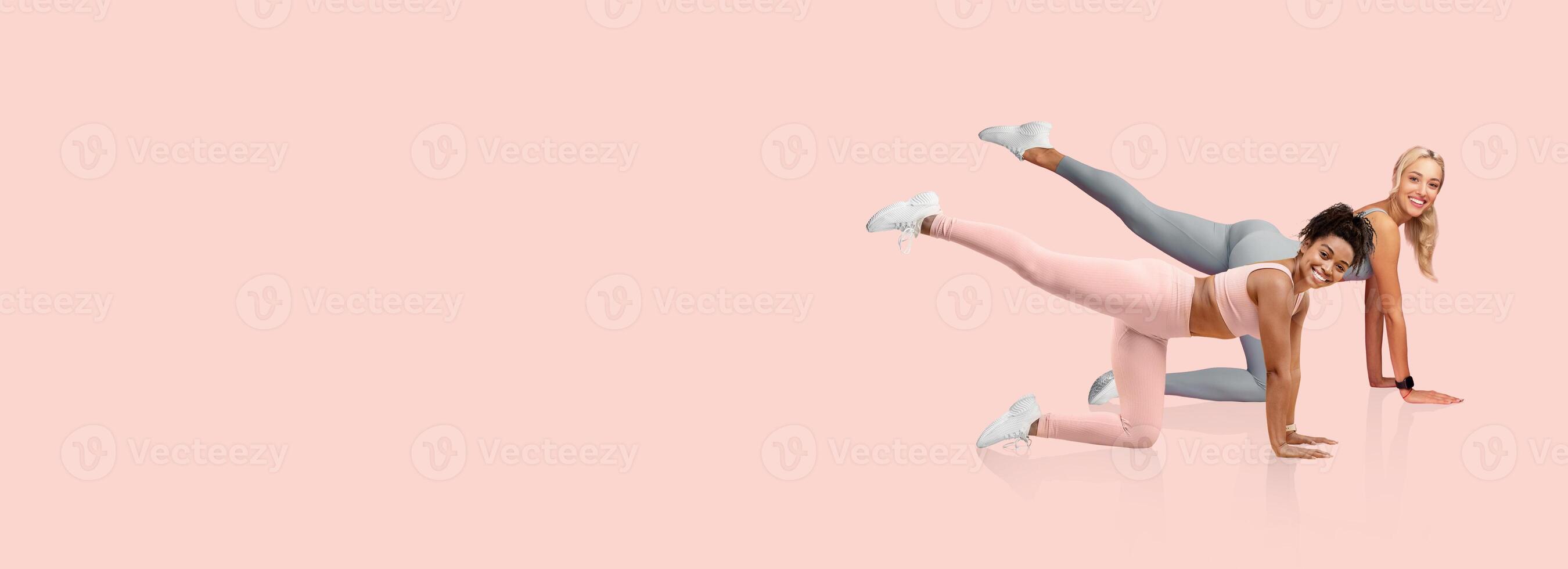 Two women perform leg lifts on hands and knees, showcasing fitness routines on a soft pink background. They're engaged in a healthy activity, promoting physical wellness and strength. photo
