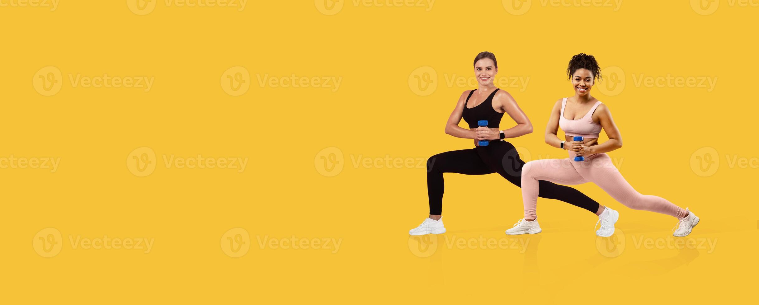 Two women engage in a lunge exercise while holding dumbbells. They are dressed in athletic wear and display focused expressions, set against a vibrant yellow background. photo
