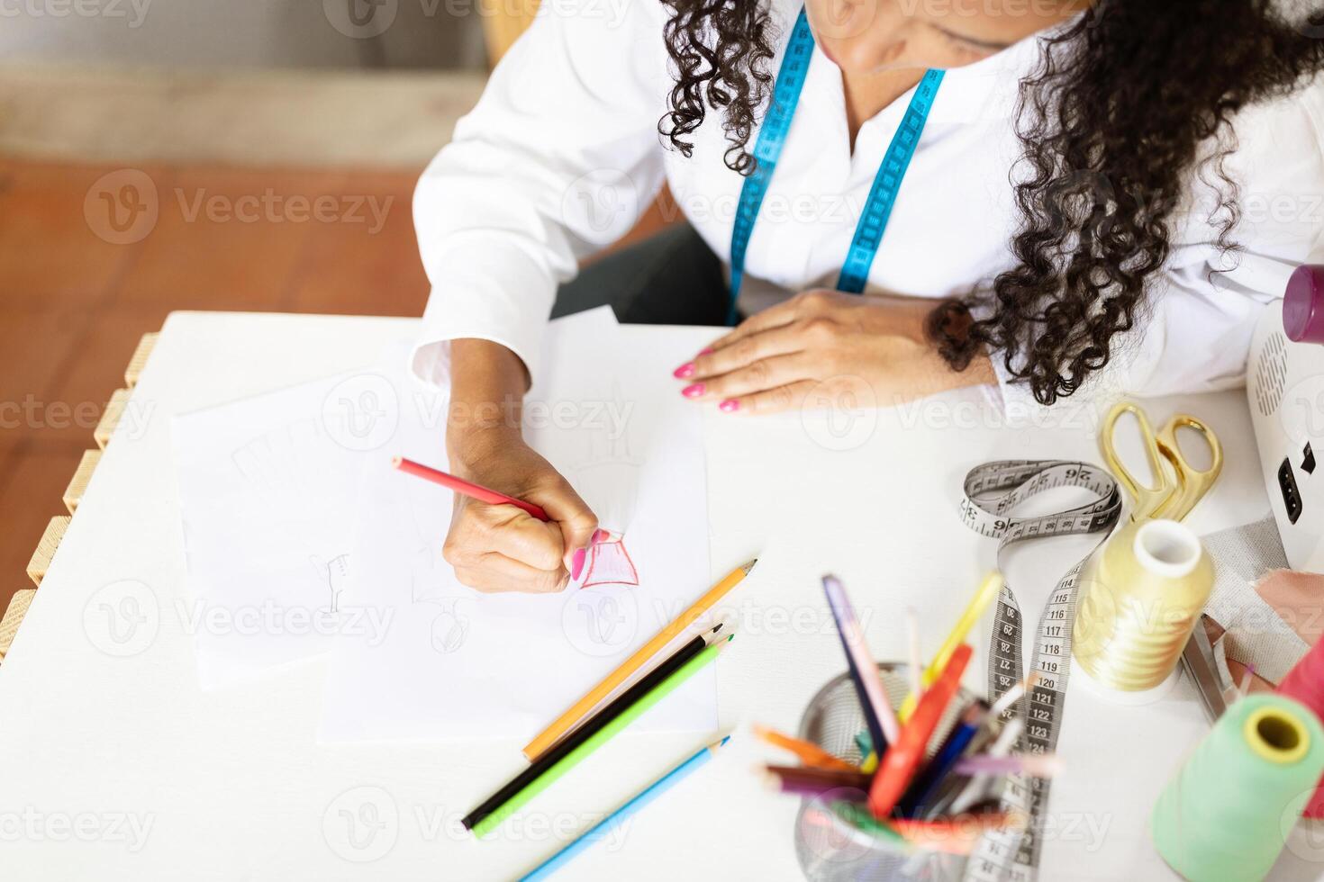 Middle aged woman works attentively at her office desk, sketching designs with colored pencils. Tools and materials are organized around her, showcasing her creative process. photo