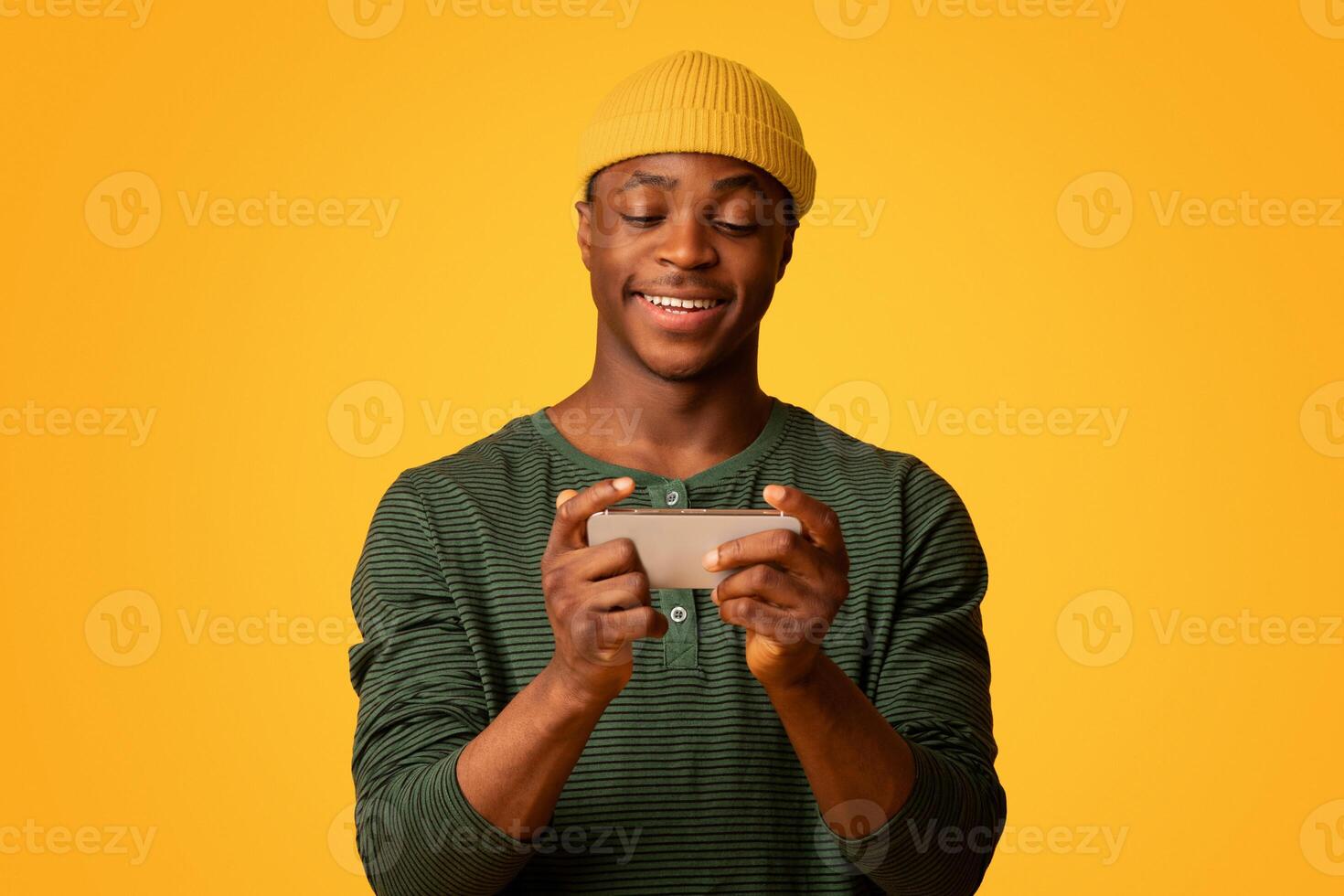 Mobile Gaming Concept. Excited Young Black Guy Playing Online Games On Smartphone, Cheerful African American Man Having Fun With Mobile Phone While Standing Over Yellow Studio Background, Free Space photo