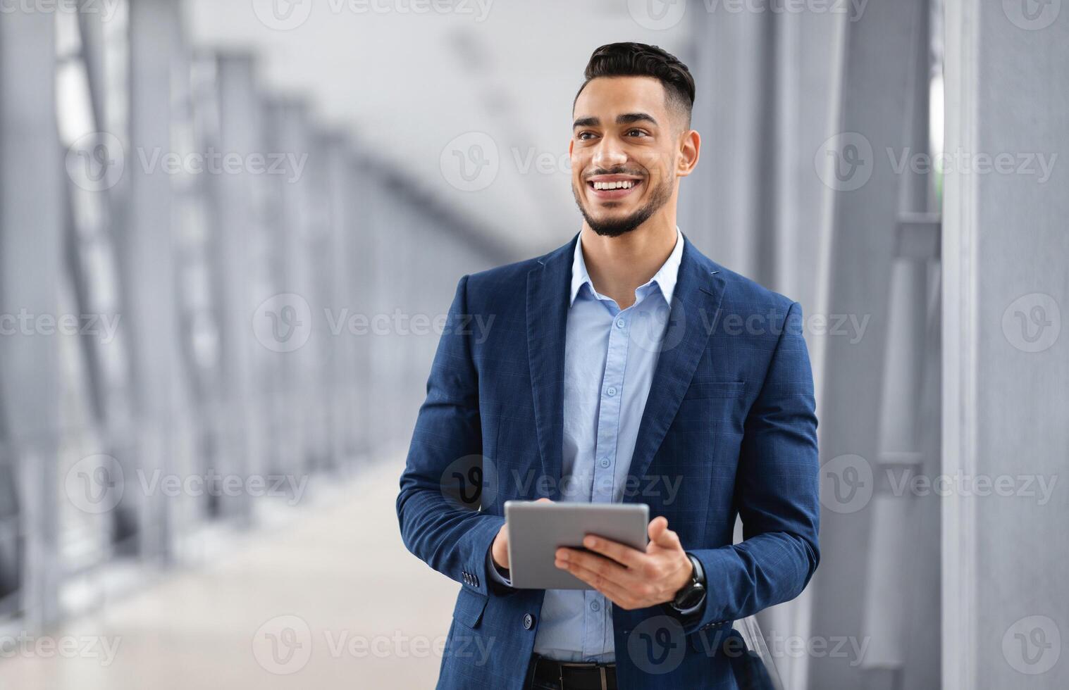 Portrait Of Happy Arab Man With Digital Tablet Standing At Airport Terminal, Handsome Middle Eastern Businessman Using Tab Computer While Waiting For Flight Departure, Enjoying Business Trip photo