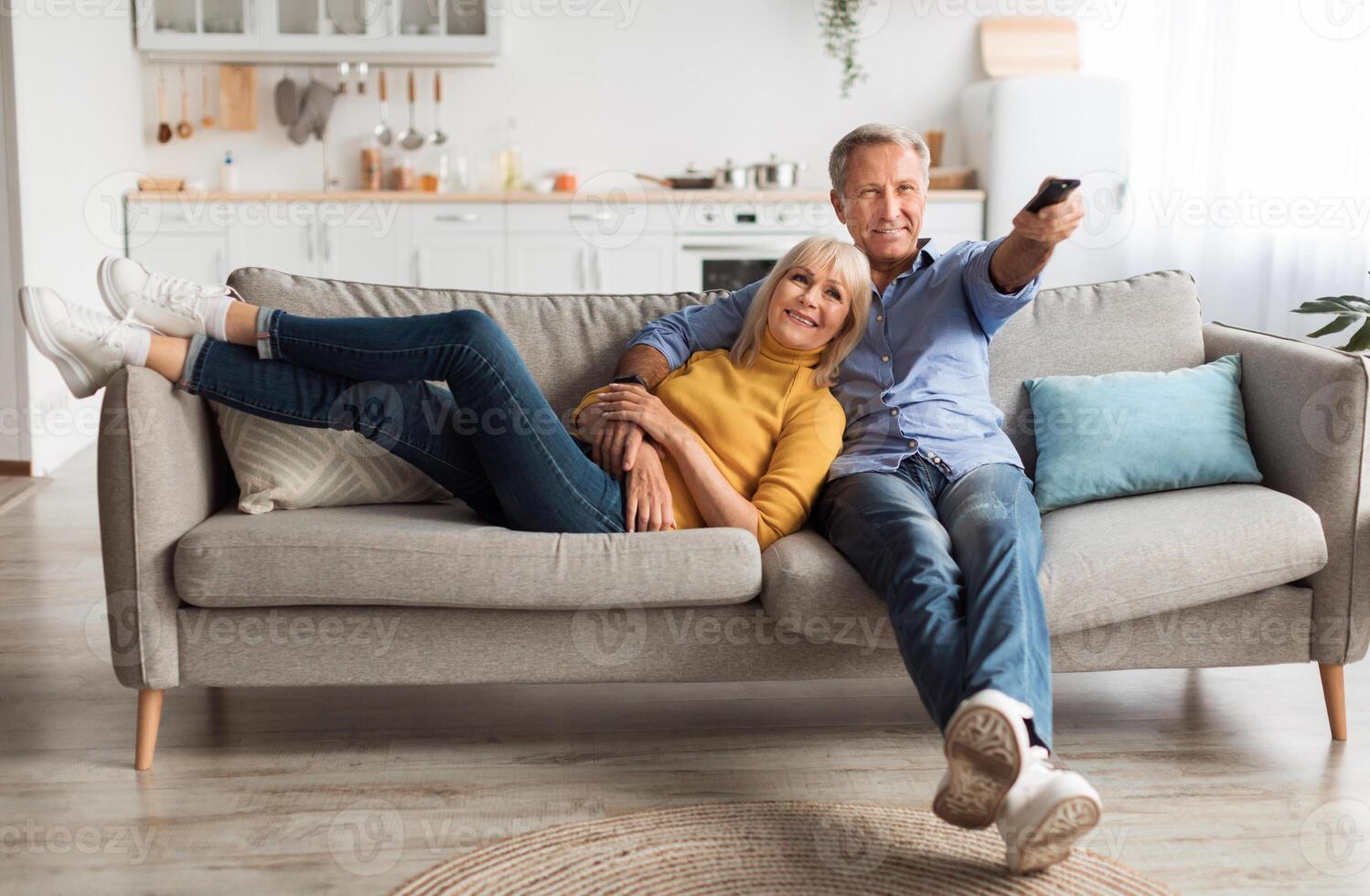 Relaxed Senior Couple Watching Television Together Sitting On Sofa And Pointing Remote Controller Switching Channels Relaxing At Home On Weekend. TV Programming Concept photo