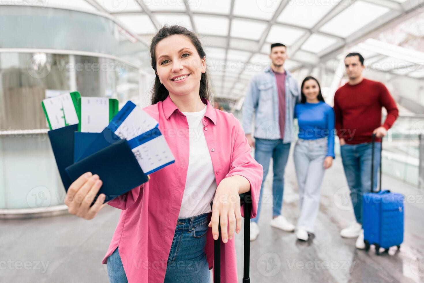 A couple stands at the airport, smiling joyfully while holding travel tickets. Friends stand nearby, all set for an exciting weekend getaway together, filled with fun and adventure. photo