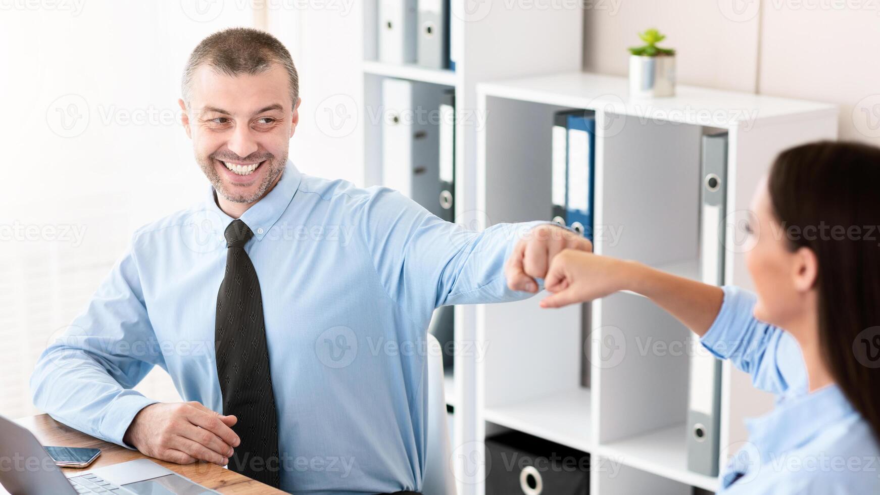 Teamwork And Partnership. Happy Coworkers Bumping Fists Celebrating Business Success At Work Sitting In Modern Office. photo