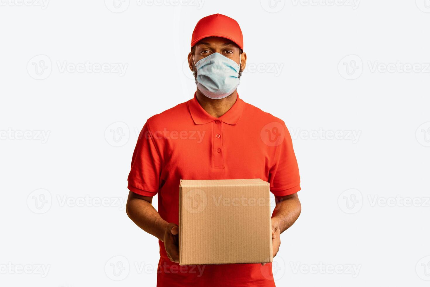 Delivery Service. Black Courier Guy Delivering Cardboard Box Holding Package Wearing Mask During Coronavirus Quarantine Standing Over Yellow Studio Background. photo