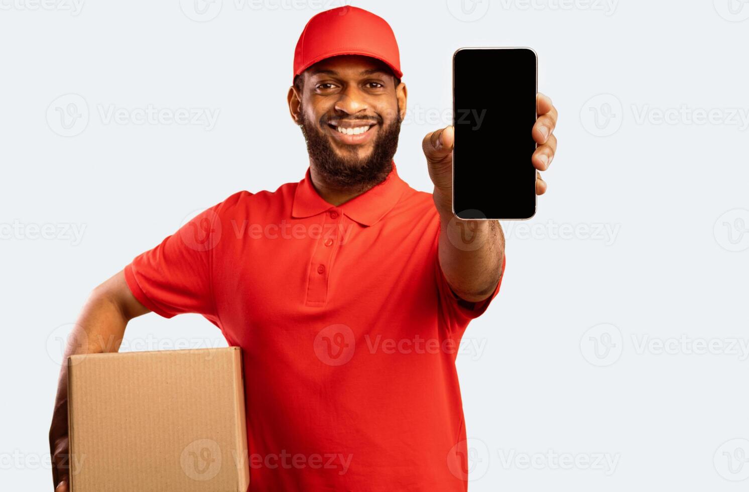 African Courier Guy Showing Smartphone With Blank Screen Holding Box Recommending Delivery Service And Online Shopping App On Yellow Background photo