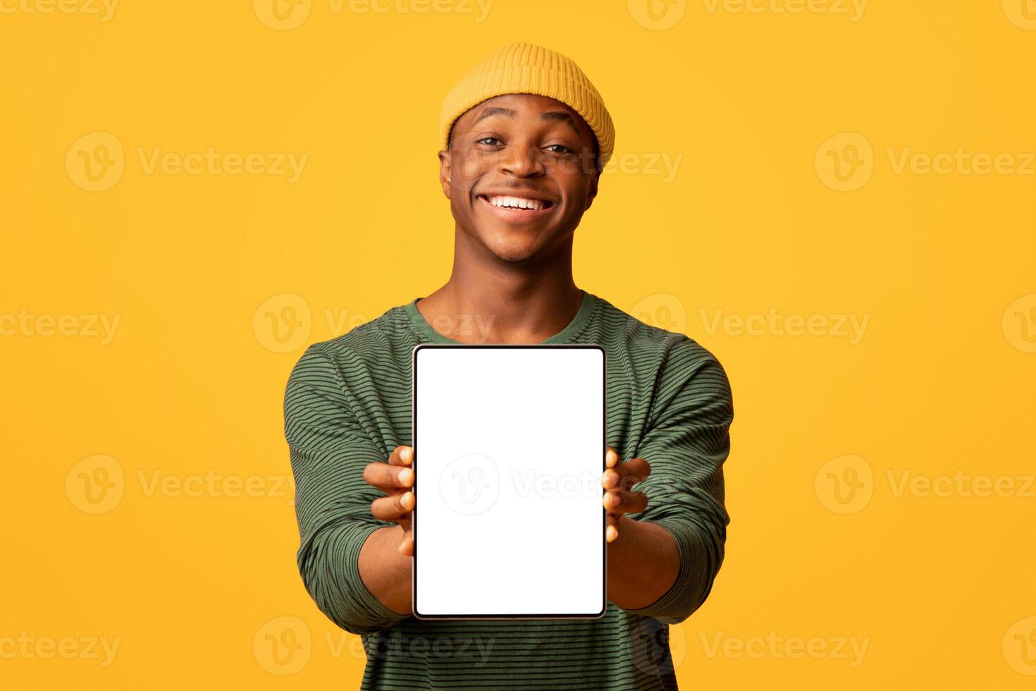 Joyful Black Hipster Guy Demonstrating Digital Tablet With White Blank Screen, Cheerful African American Man Recommending New App Or Website While Standing Isolated Over Yellow Background, Copy Space photo