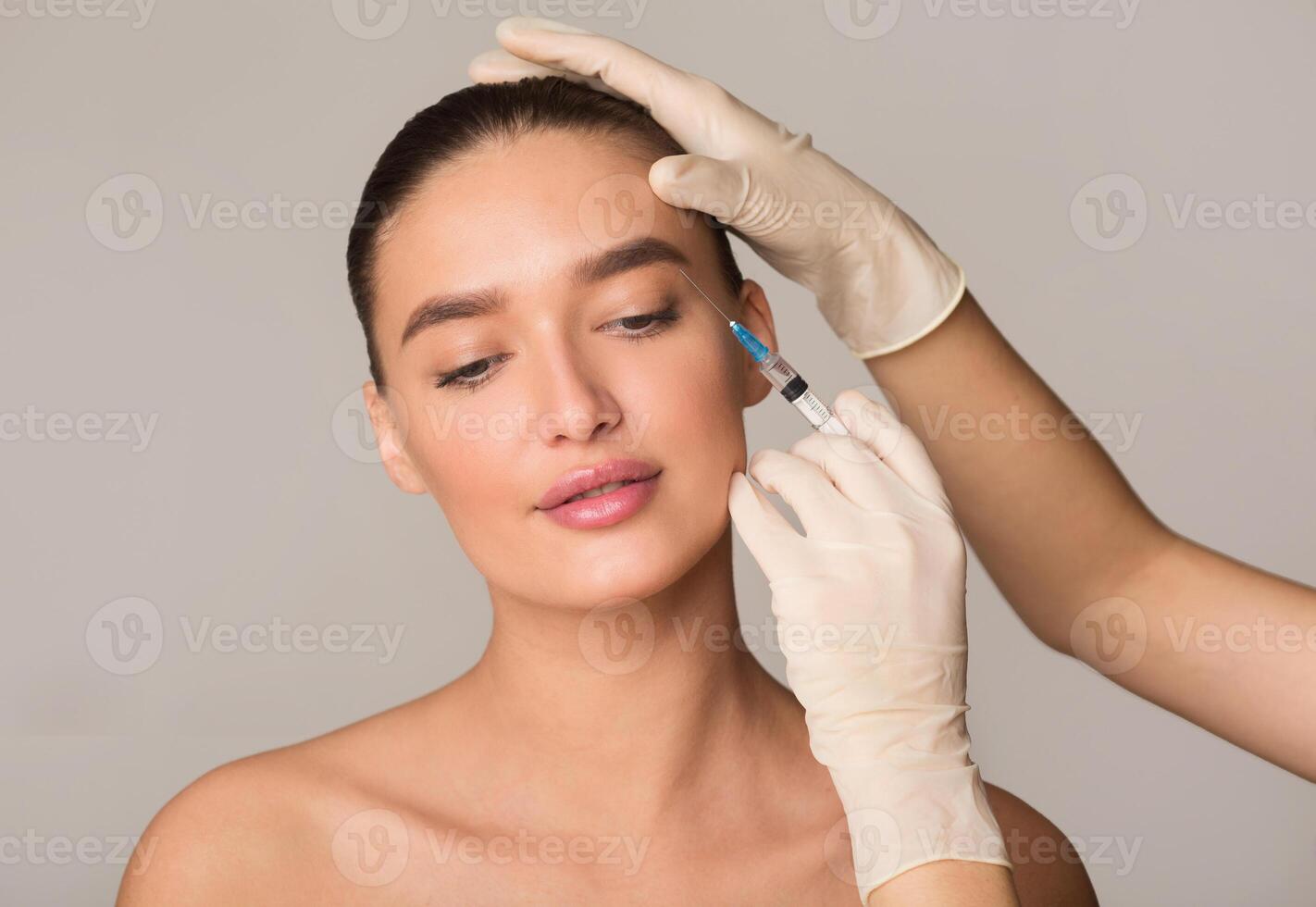 Plastic Surgery And Beauty Injection Concept. Young Woman Receiving Botox For Wrinkles, Isolated Over Studio Wall photo