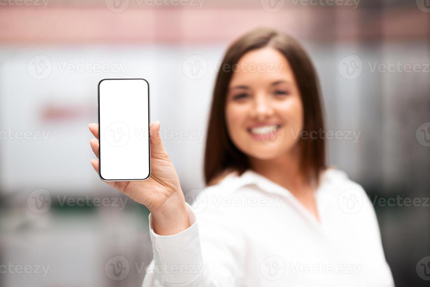 A millennial businesswoman is smiling confidently as she holds a smartphone in an office. The modern workspace features sleek furniture and a professional atmosphere, ideal for collaboration. photo