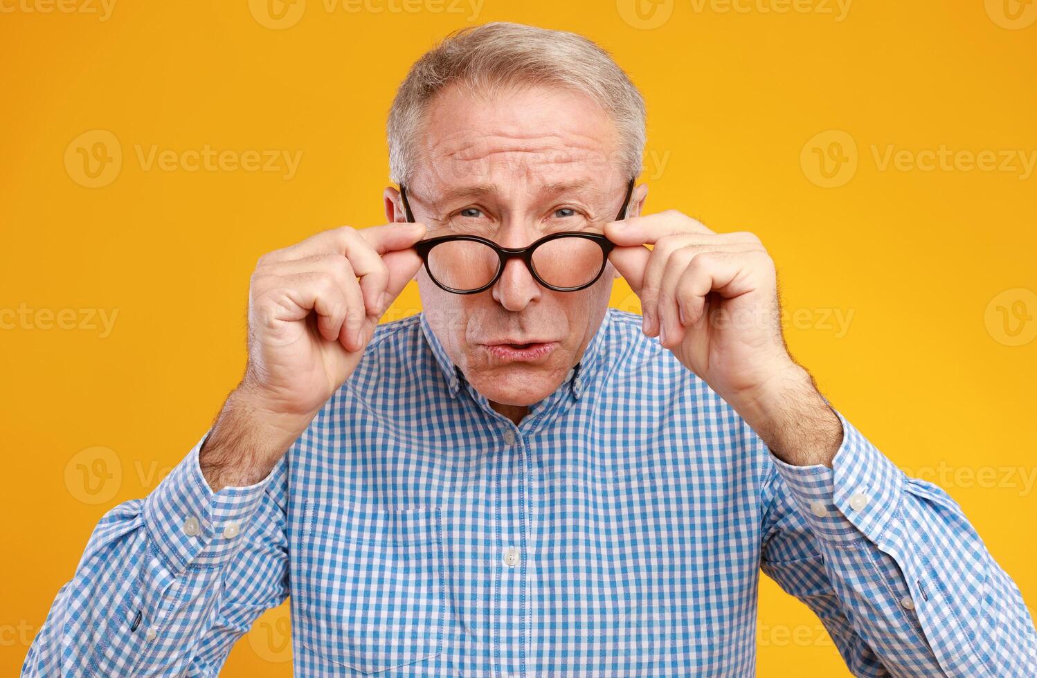 Poor Eyesight. Senior Man Can't See, Squinting Eyes Wearing Eyeglasses Having Problems With Vision, Looking At Camera, Yellow Orange Wall. Ophtalmic Issue In Older Age, Macular Degeneration Concept photo