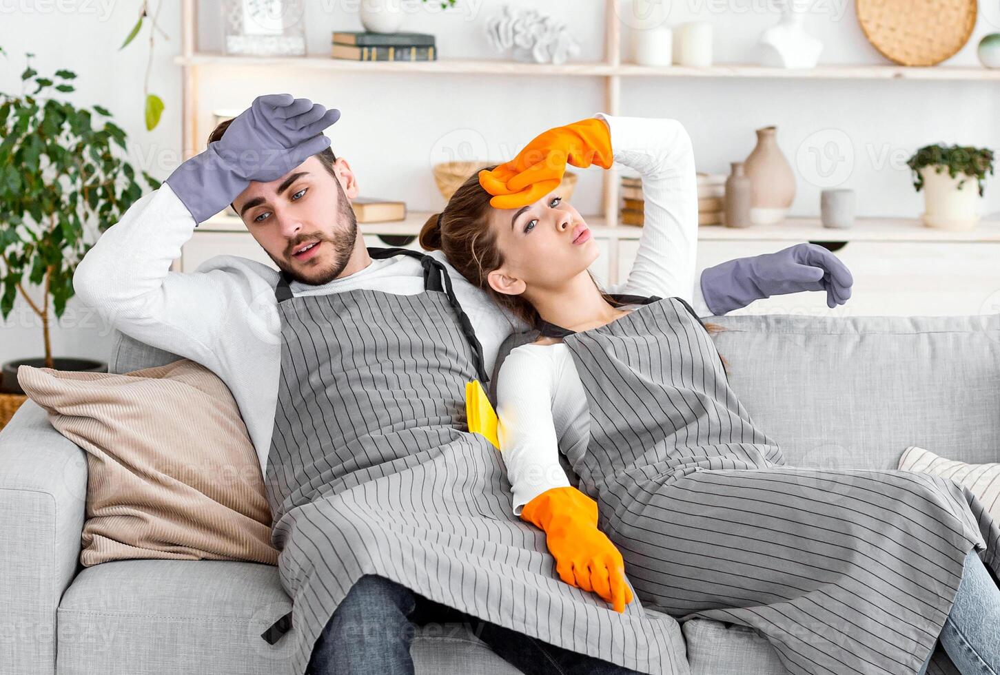Tired after cleaning. Husband and wife are resting on couch, wiping sweat from forehead. photo