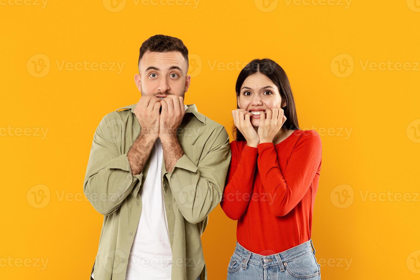 A young Caucasian couple stands together with playful expressions, showing surprise and excitement. They are isolated against a bright yellow background, enhancing their cheerful demeanor. photo