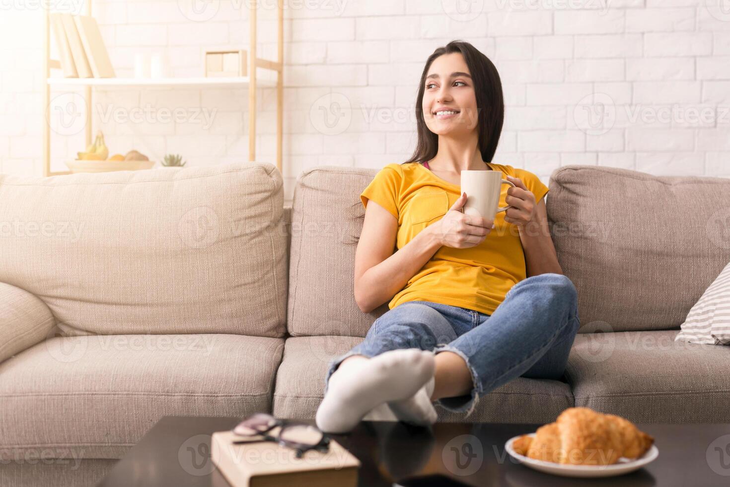 Lazy morning at home. Smiling girl with cup of hot drink relaxing on sofa indoors, copy space photo