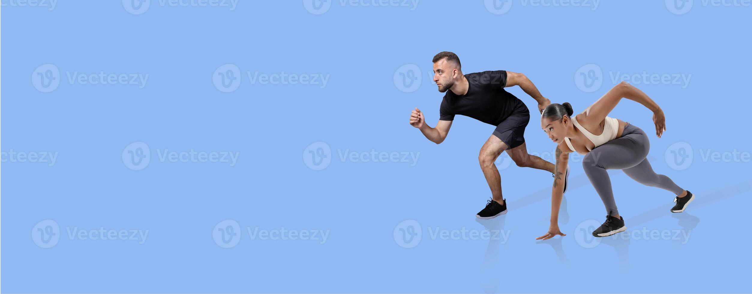 A man and woman are positioned in a starting stance for a sprint. They are both focused and energized, showcasing a collaborative workout session. The simple blue background enhances their movements. photo