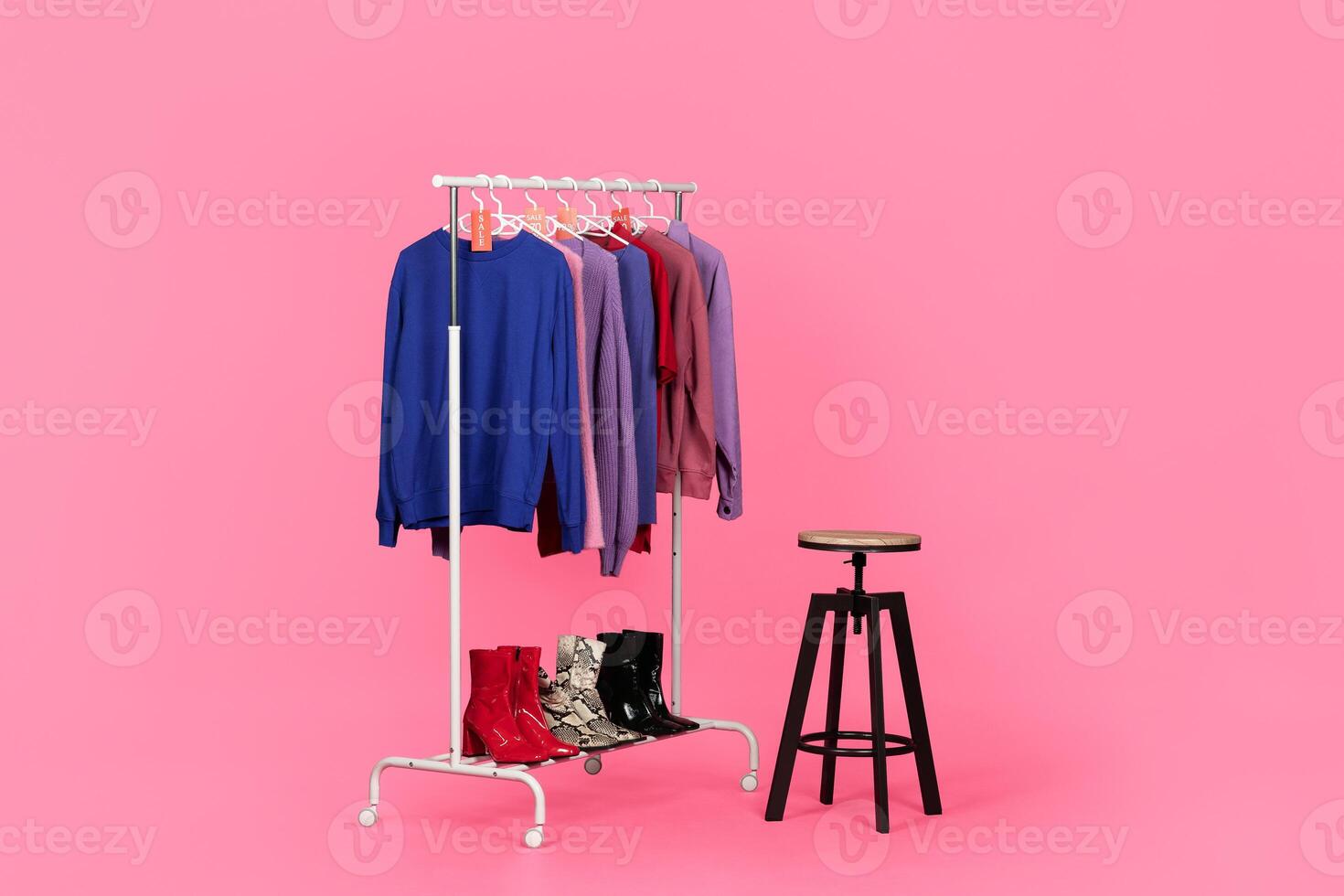 Stylish clothing and boots on a rack. Symbol of modern consumerism while shopping for trendy outfits, pink studio background photo
