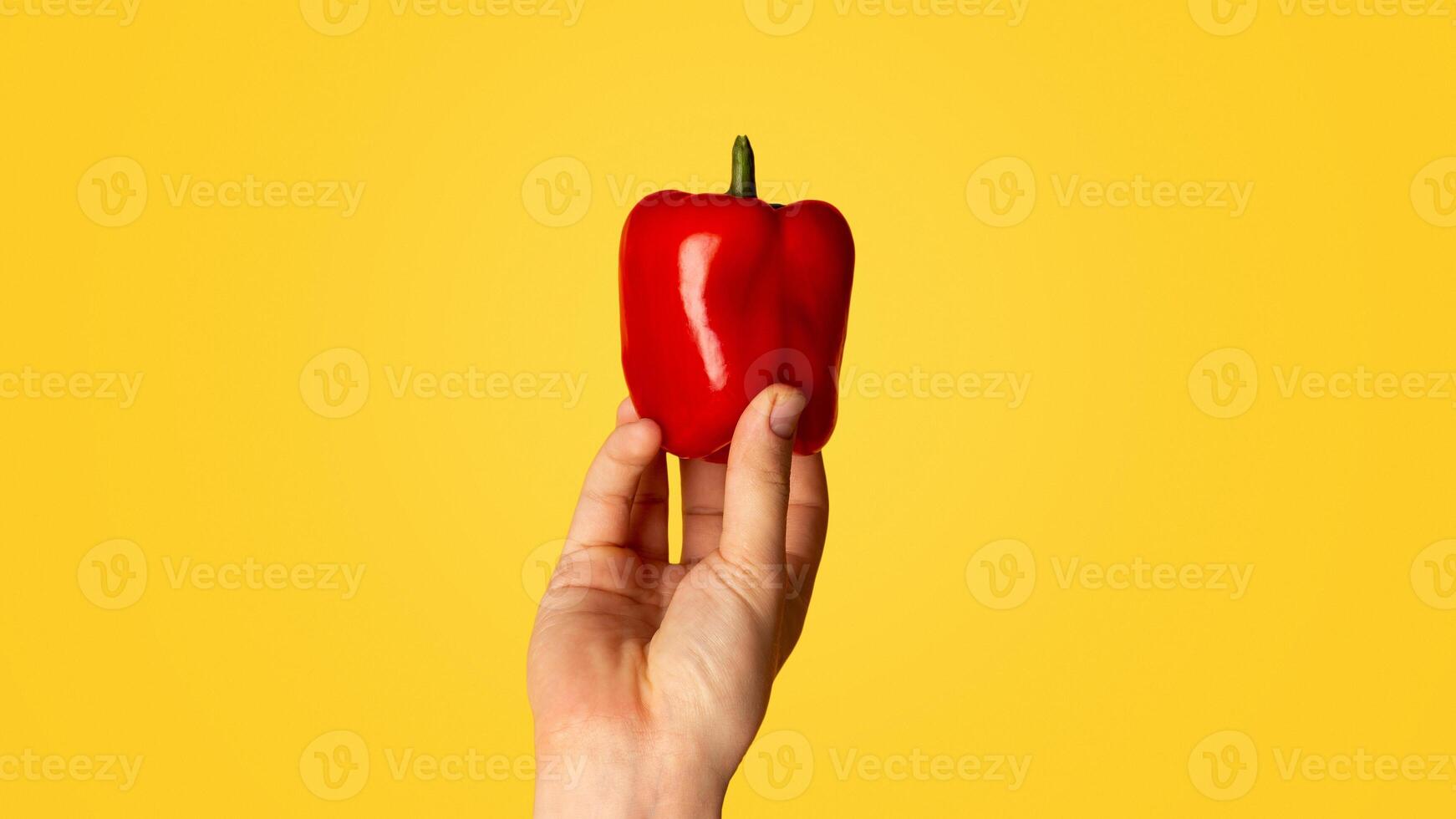 Closeup of male hand showing red bell pepper on orange background photo