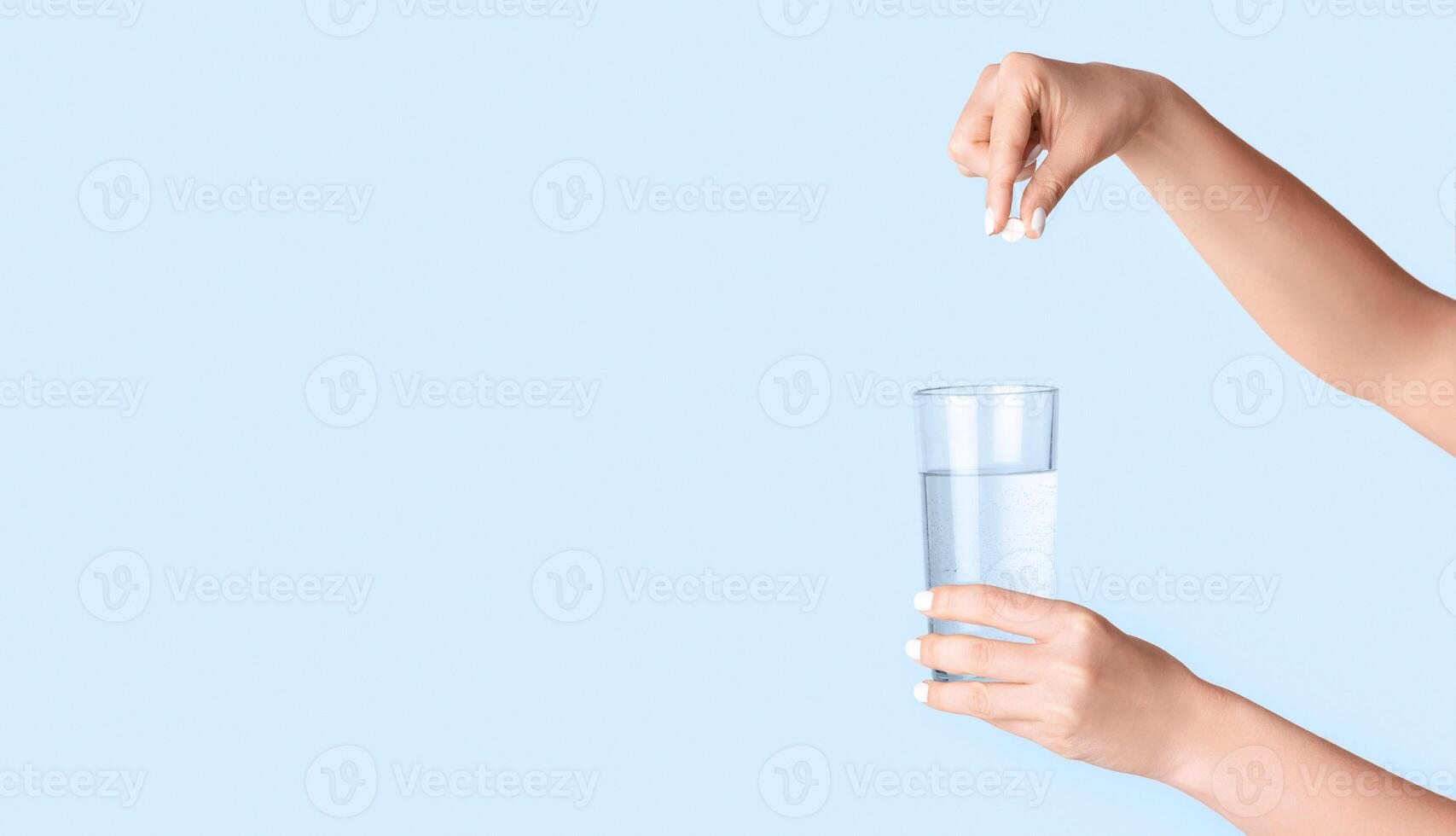 Female hands dropping pill into glass of water on light background, close up. Blank space. Panorama photo