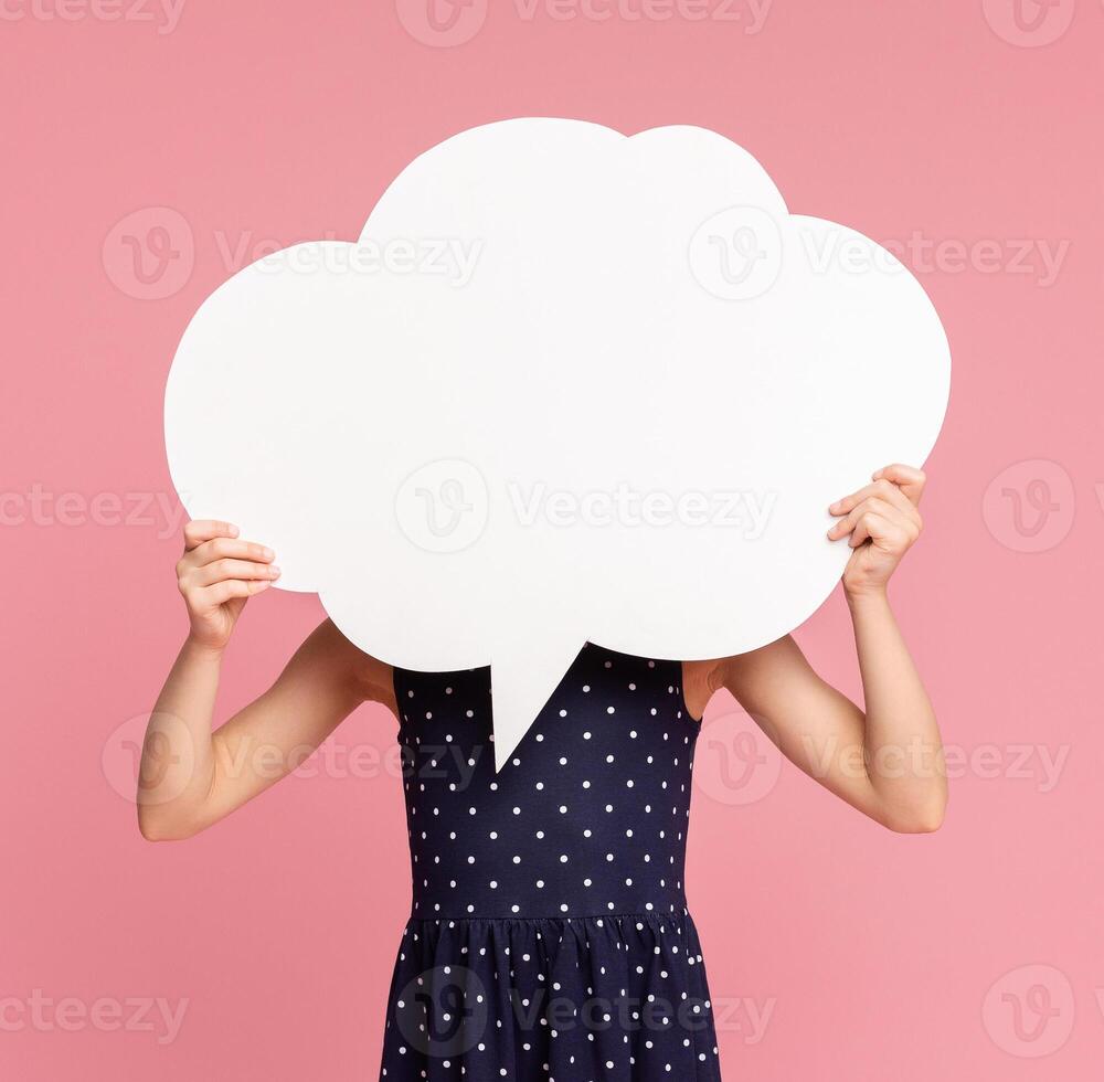 Little girl hiding her face behind blank white speech bubble, pink studio background photo