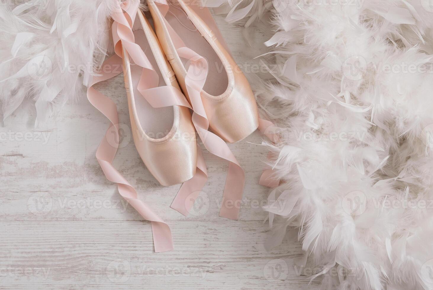 Pastel pink ballet shoes background. New pointe shoes with satin ribbon lay on white rustic shubby chic wood near feather boa, top view with copy space photo