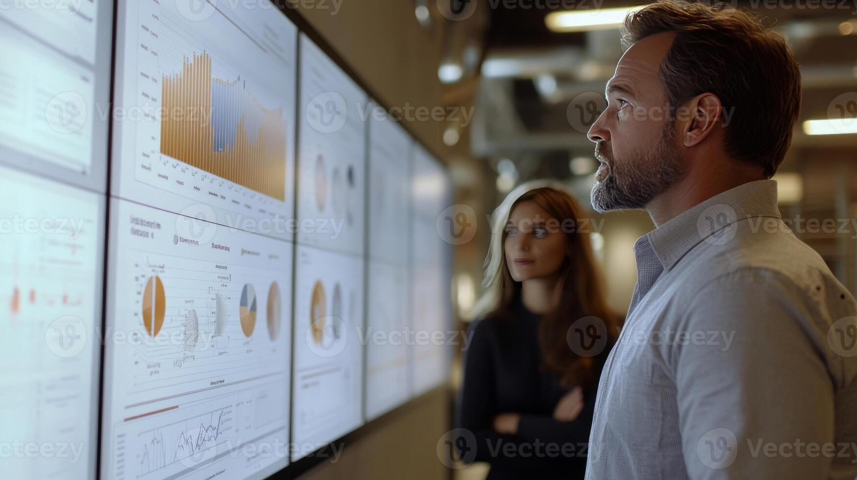 A man and woman looking at a large screen with graphs photo