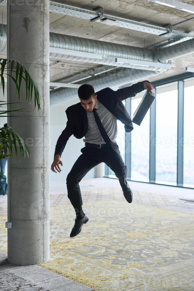 A businessman ecstatically jumping in a modern office, holding a briefcase in his hands, celebrating a moment of success and triumph. photo