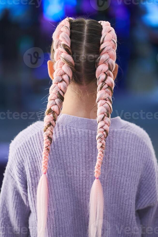 A child with pigtails made of pink kanekalon. He stands with his back to the camera, showing his braided hair. There is a place to copy photo
