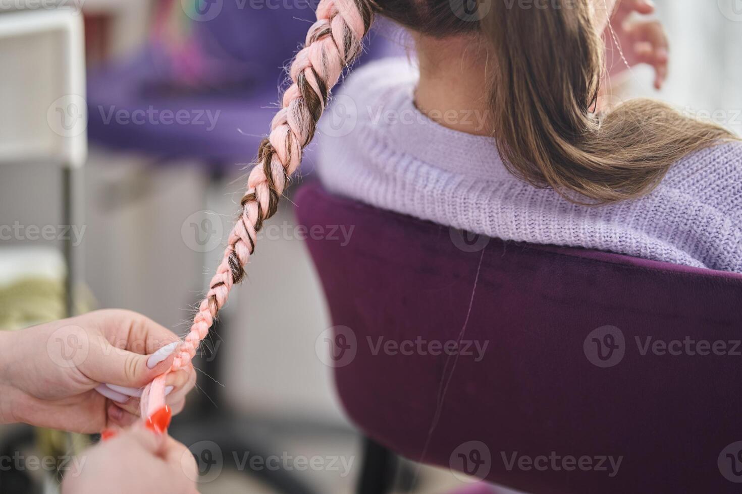 Braid pigtail made of pink kanekalon. The hands of the master who weave the kanekalon material into the hair. With space to copy photo