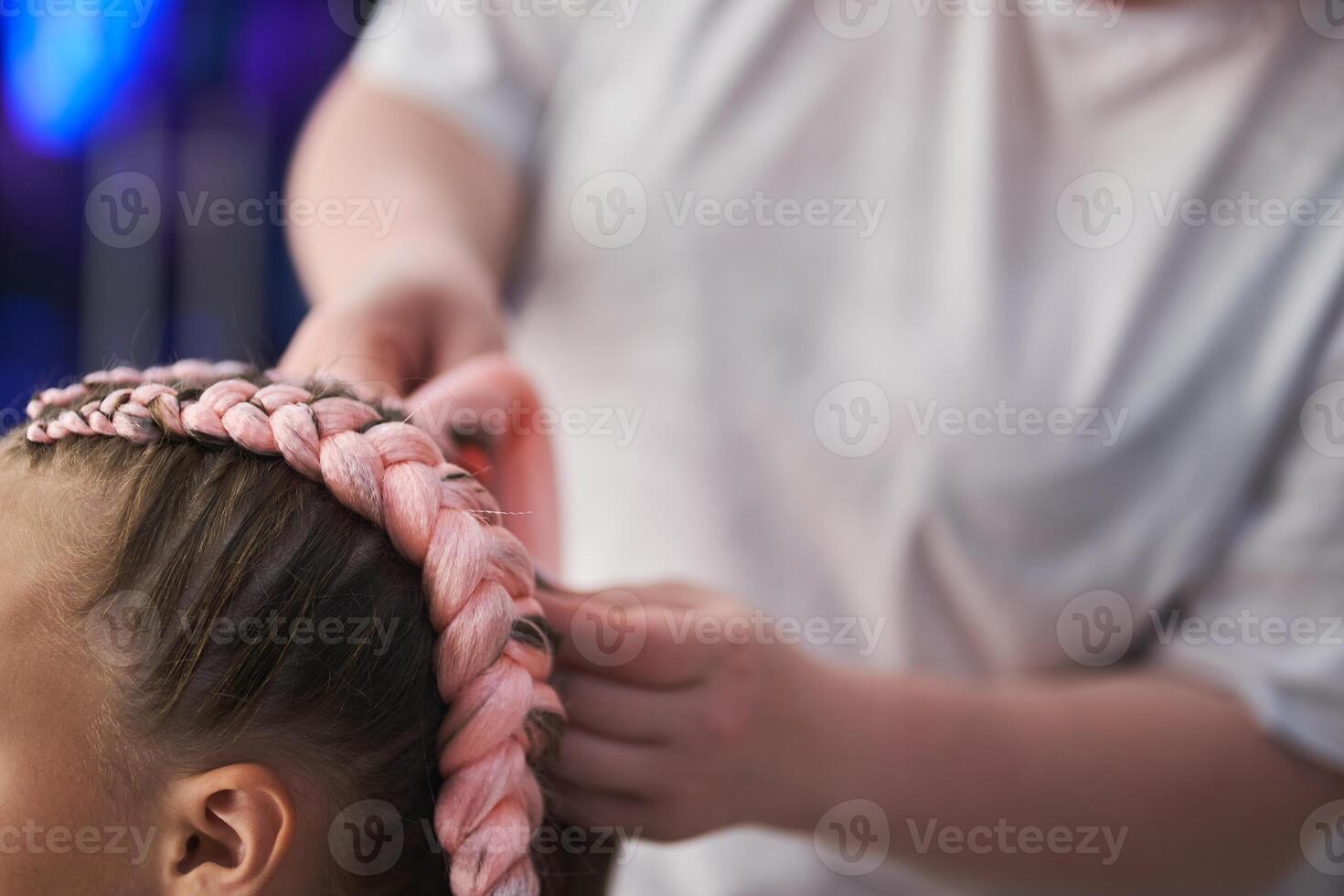 Close-up of the pigtail on the child's head made of pink kanekalon. The hands of the master who weave the kanekalon material into the hair. With space to copy photo